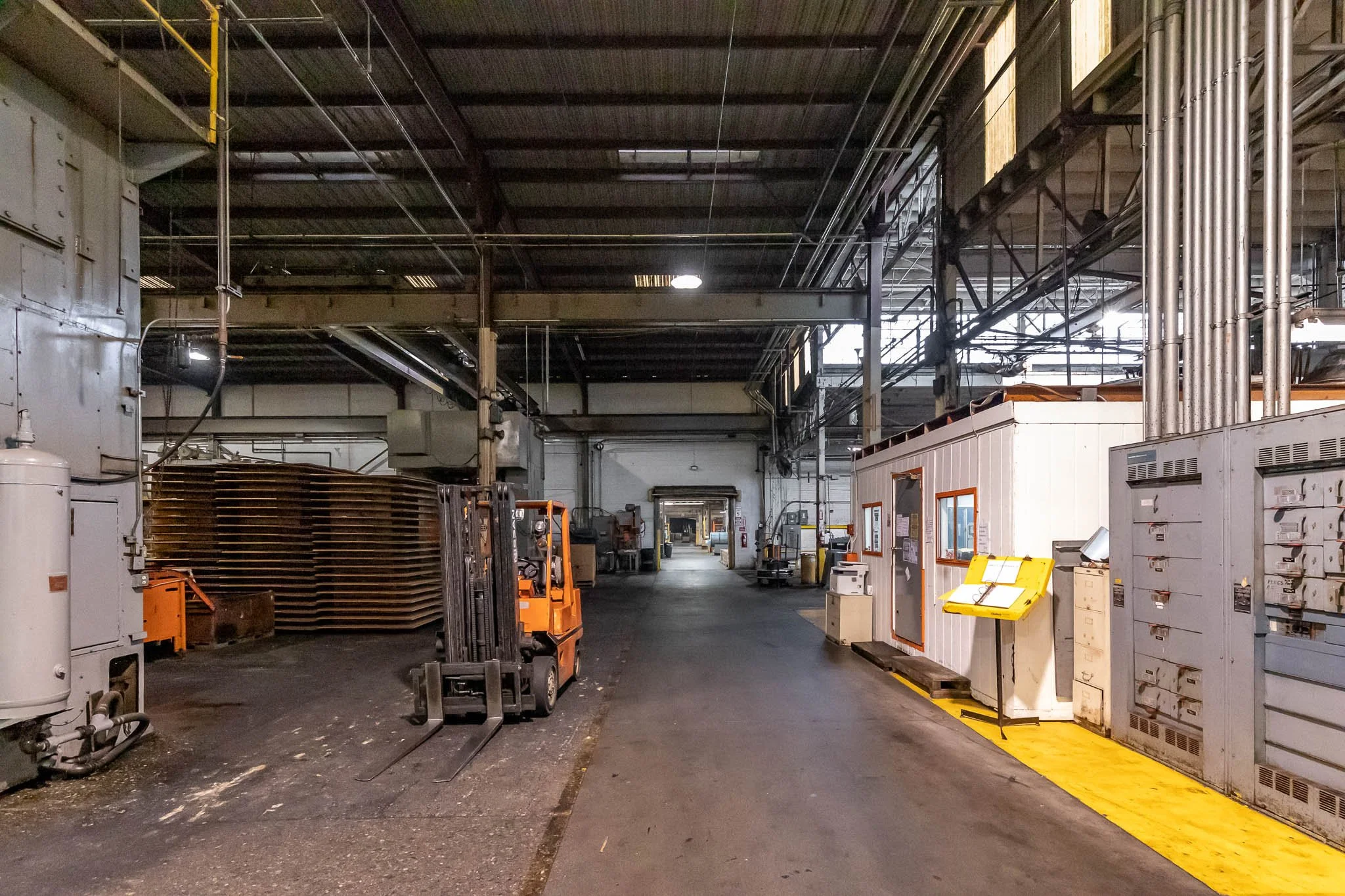 Industrial warehouse with forklift, storage racks, electrical boxes, and machinery in a large open space.