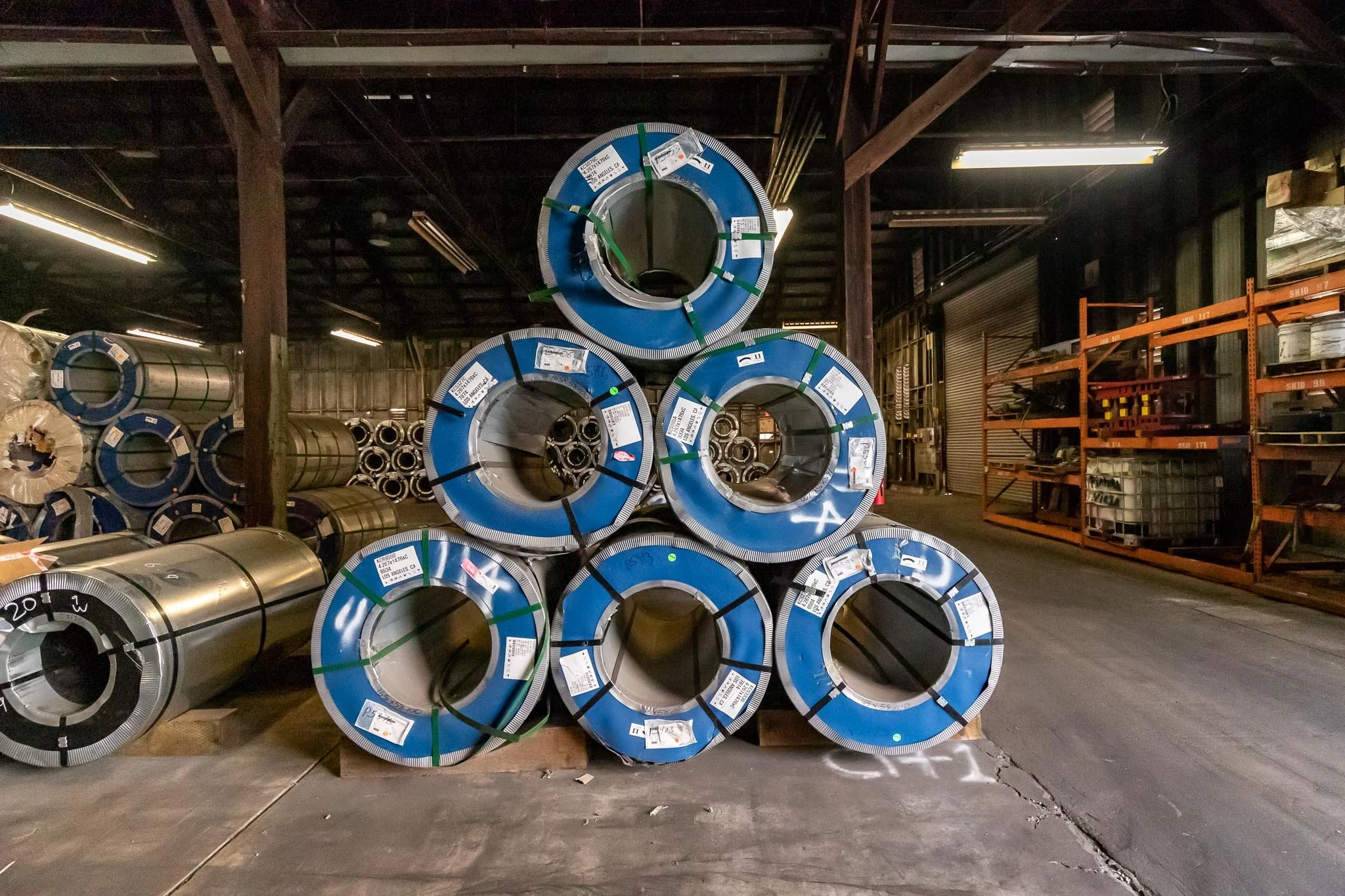 Stack of steel coils wrapped in blue plastic in an industrial warehouse.