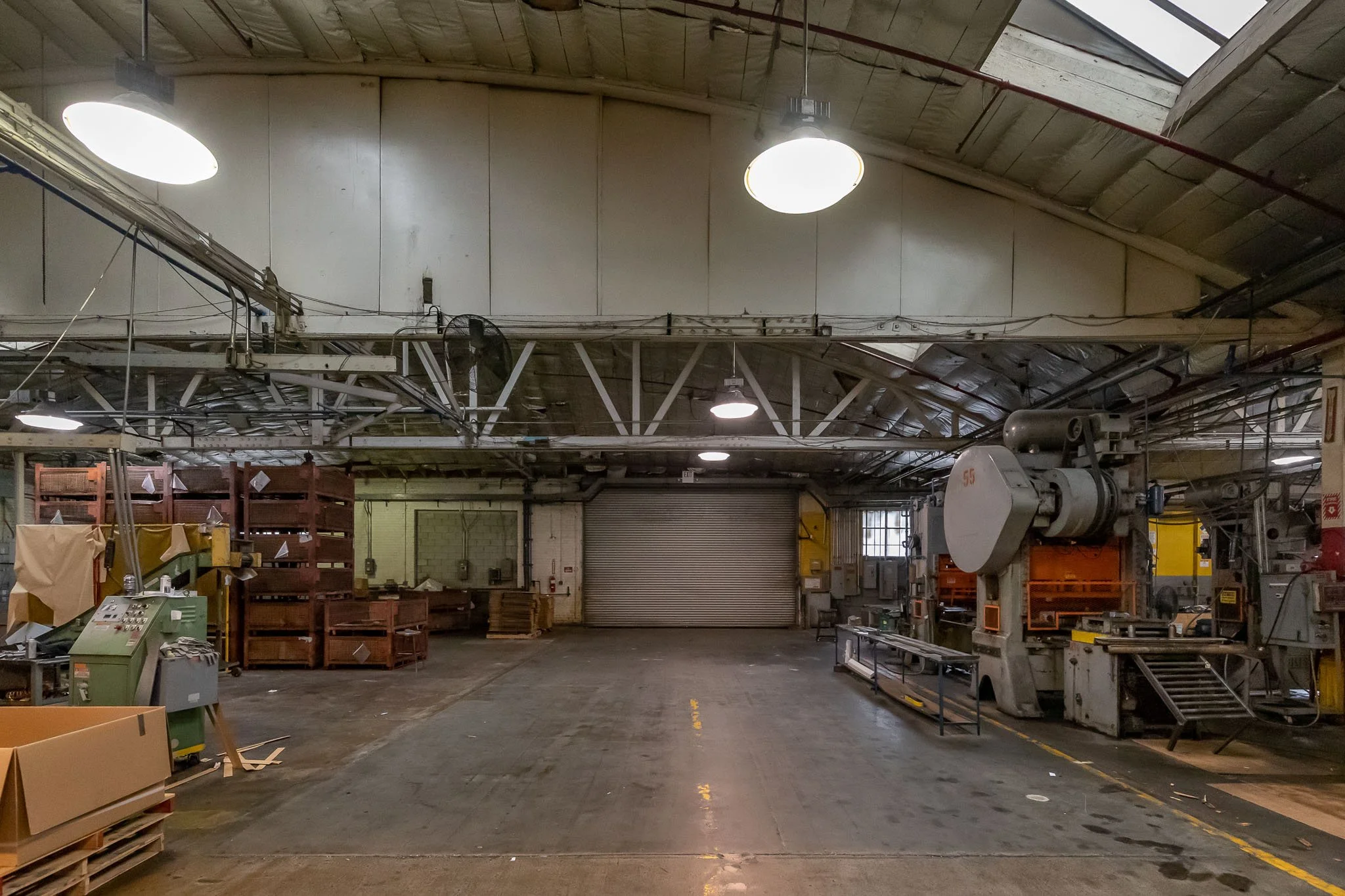 Empty industrial warehouse with machinery, shelves, and a rolling door in the background.