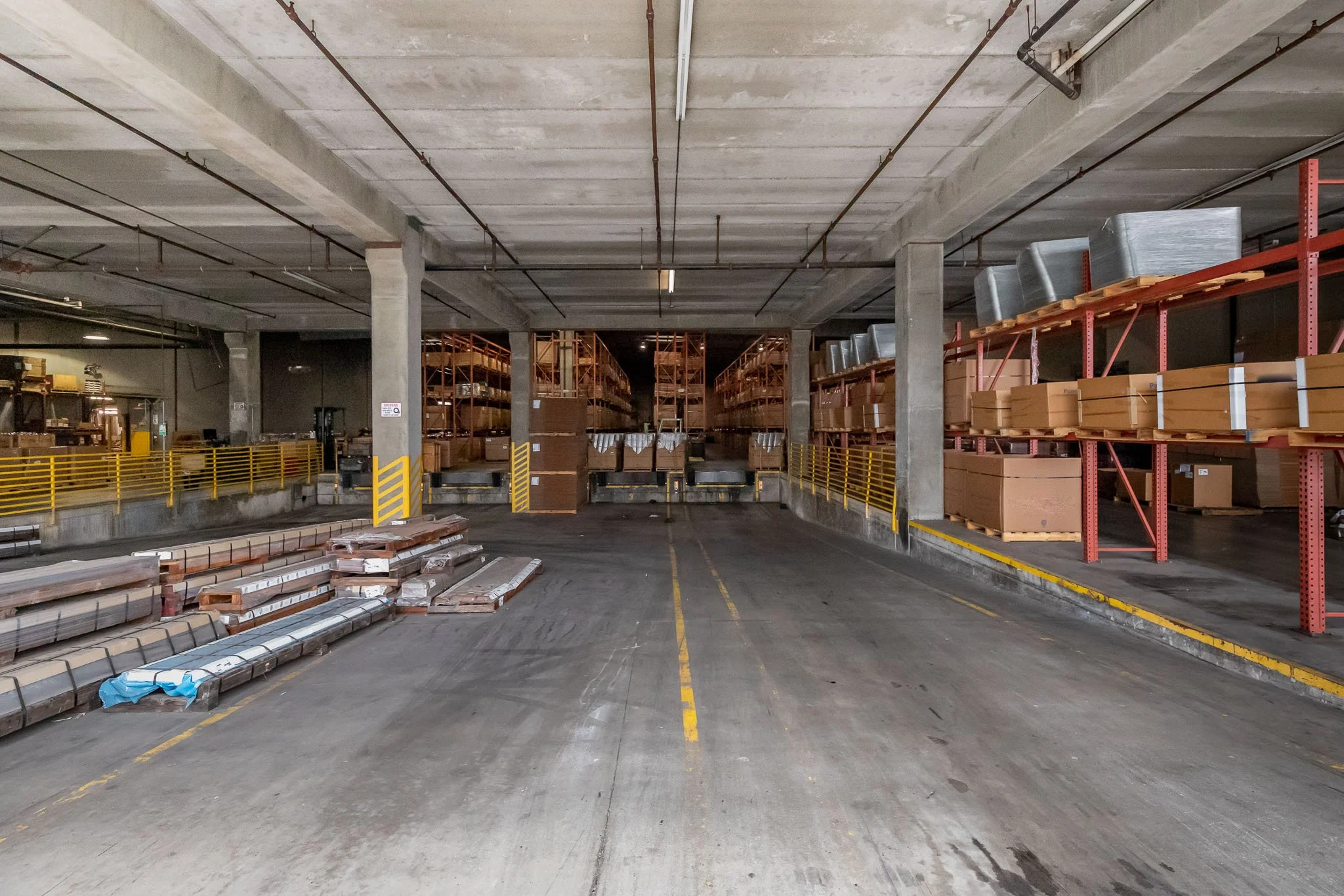 Empty warehouse parking area with stacked construction materials and shelving units on both sides.