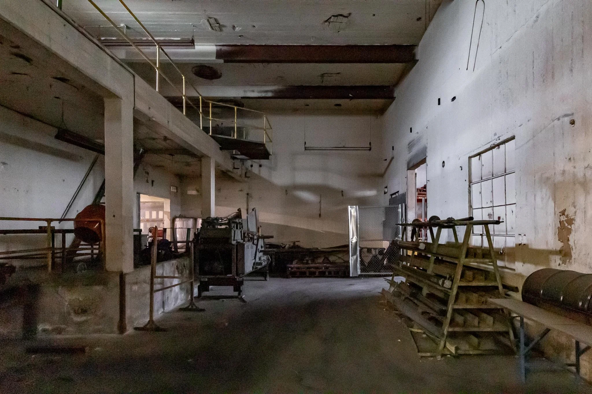Interior of an abandoned, dusty industrial building with debris, old equipment, and scaffolding, dimly lit with peeling paint on walls.
