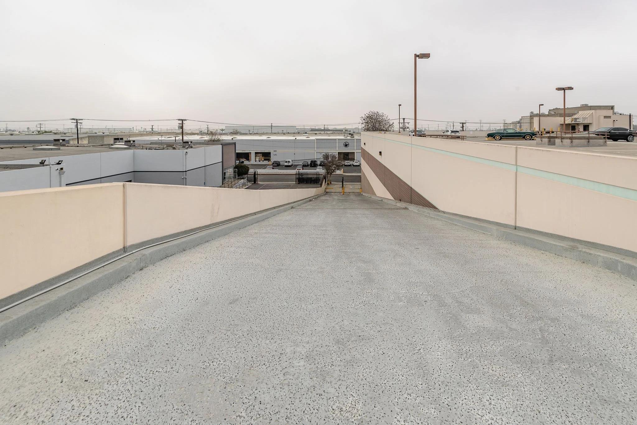 Empty rooftop parking lot with a view of commercial buildings and parked cars under gray sky.
