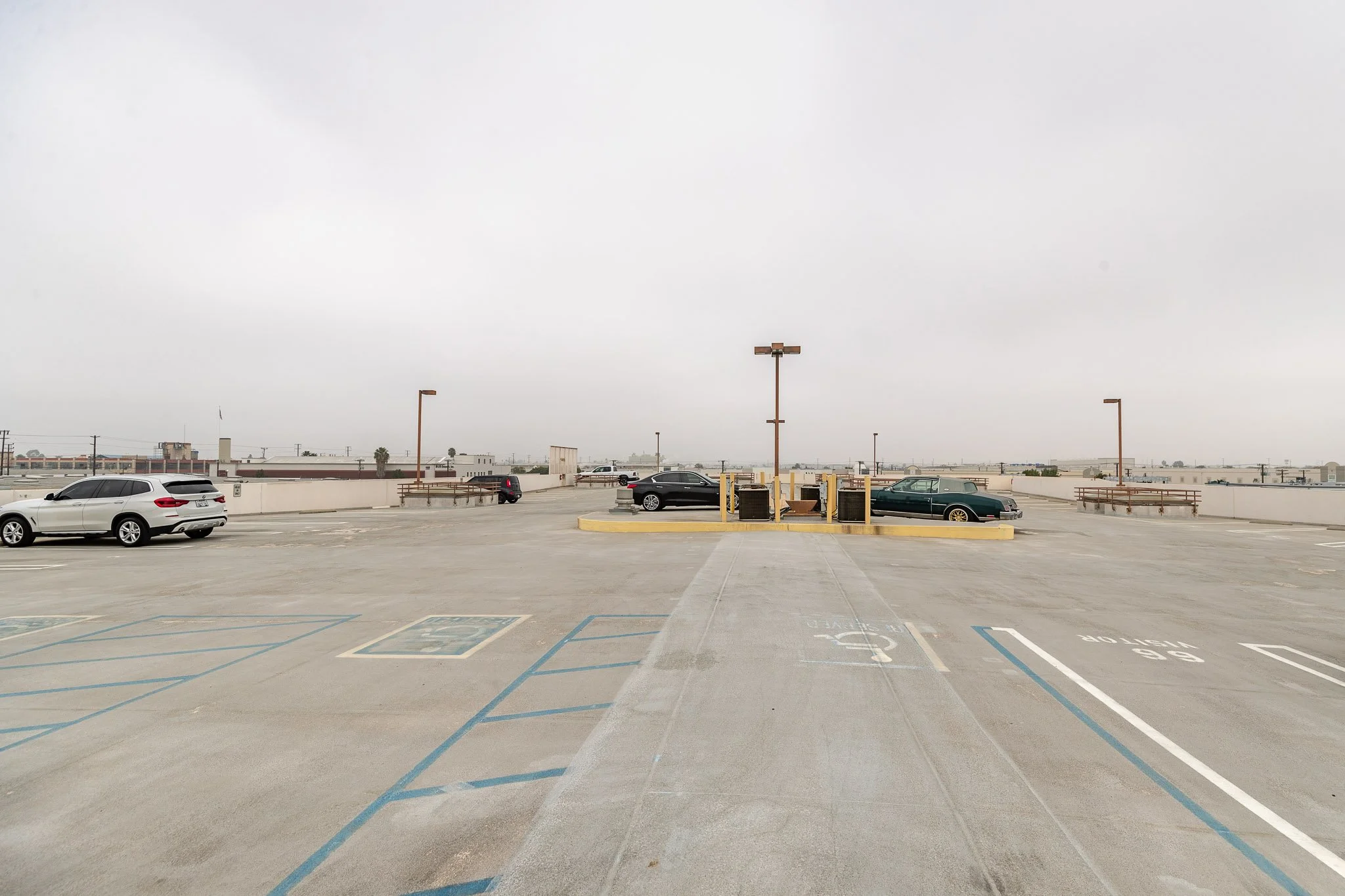 Empty rooftop parking lot on overcast day with a few parked cars and visible reach spaces.