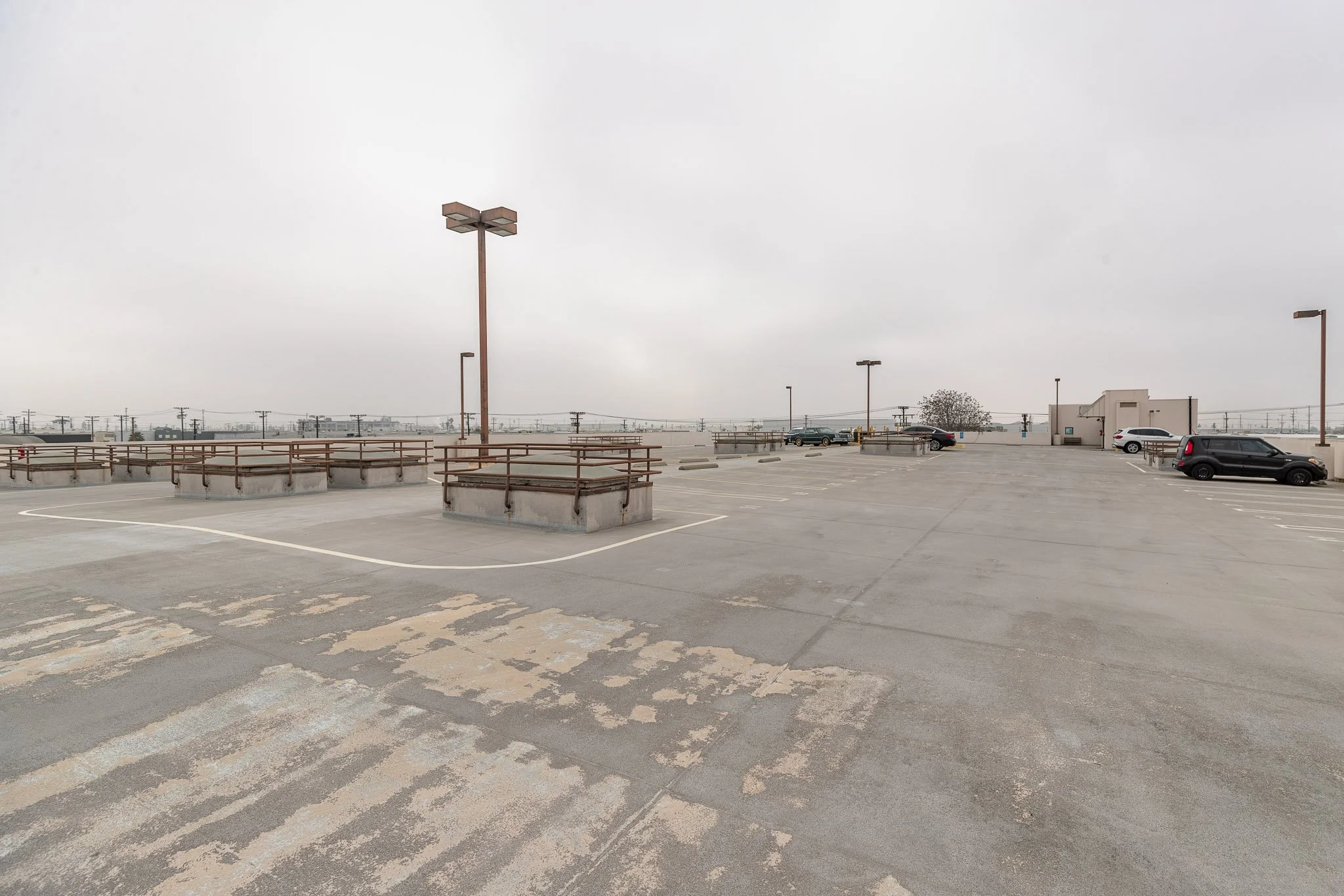Empty rooftop parking lot on a cloudy day with a few parked cars and utility poles in the distance.