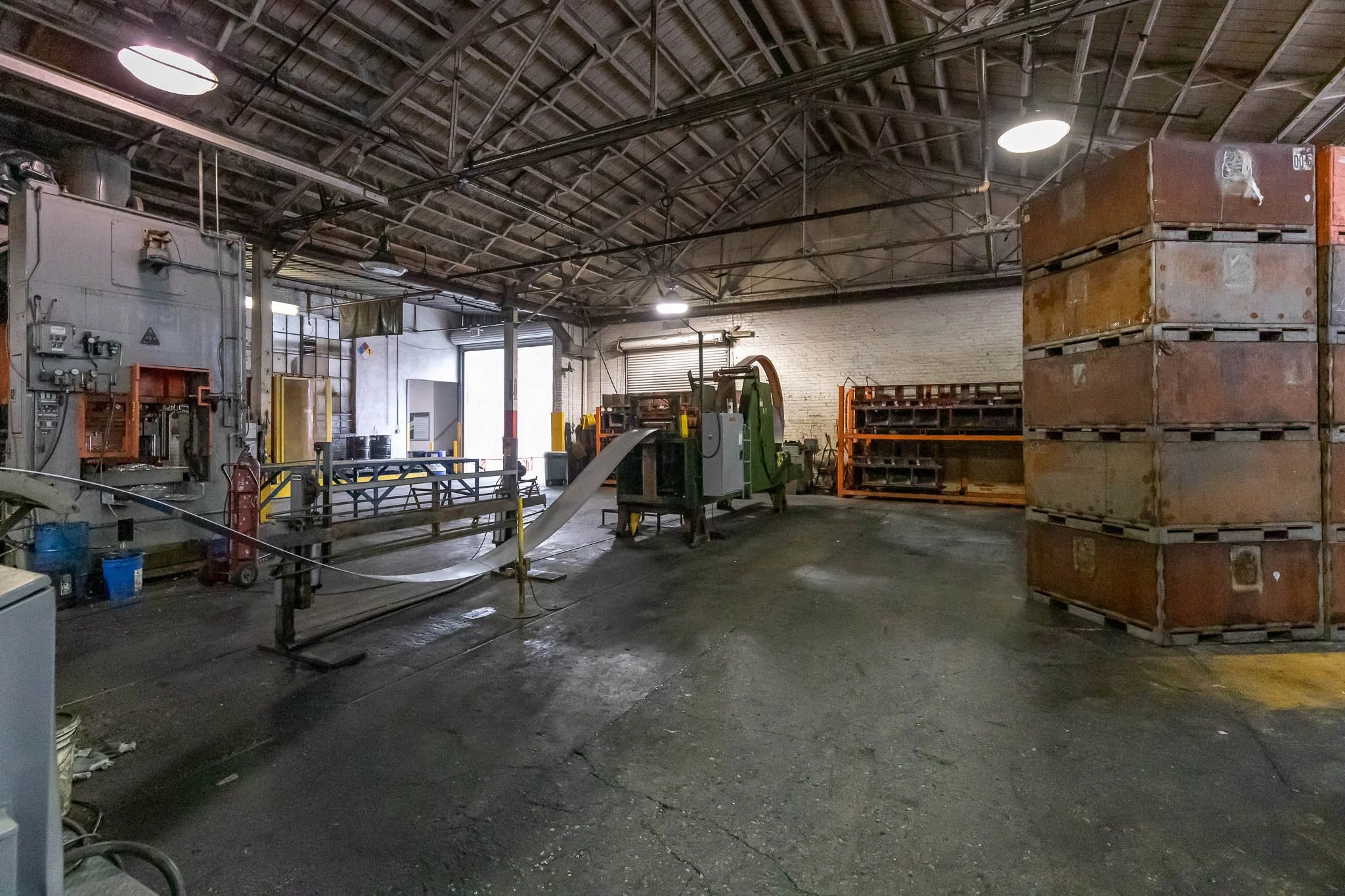 Inside an industrial warehouse with machinery, stacked containers, and open garage doors