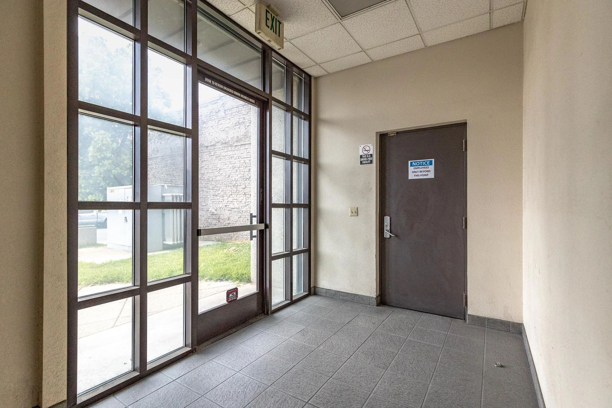 Indoor entrance area with a glass door and a solid black door, both with signs, and an exit sign above the glass door.