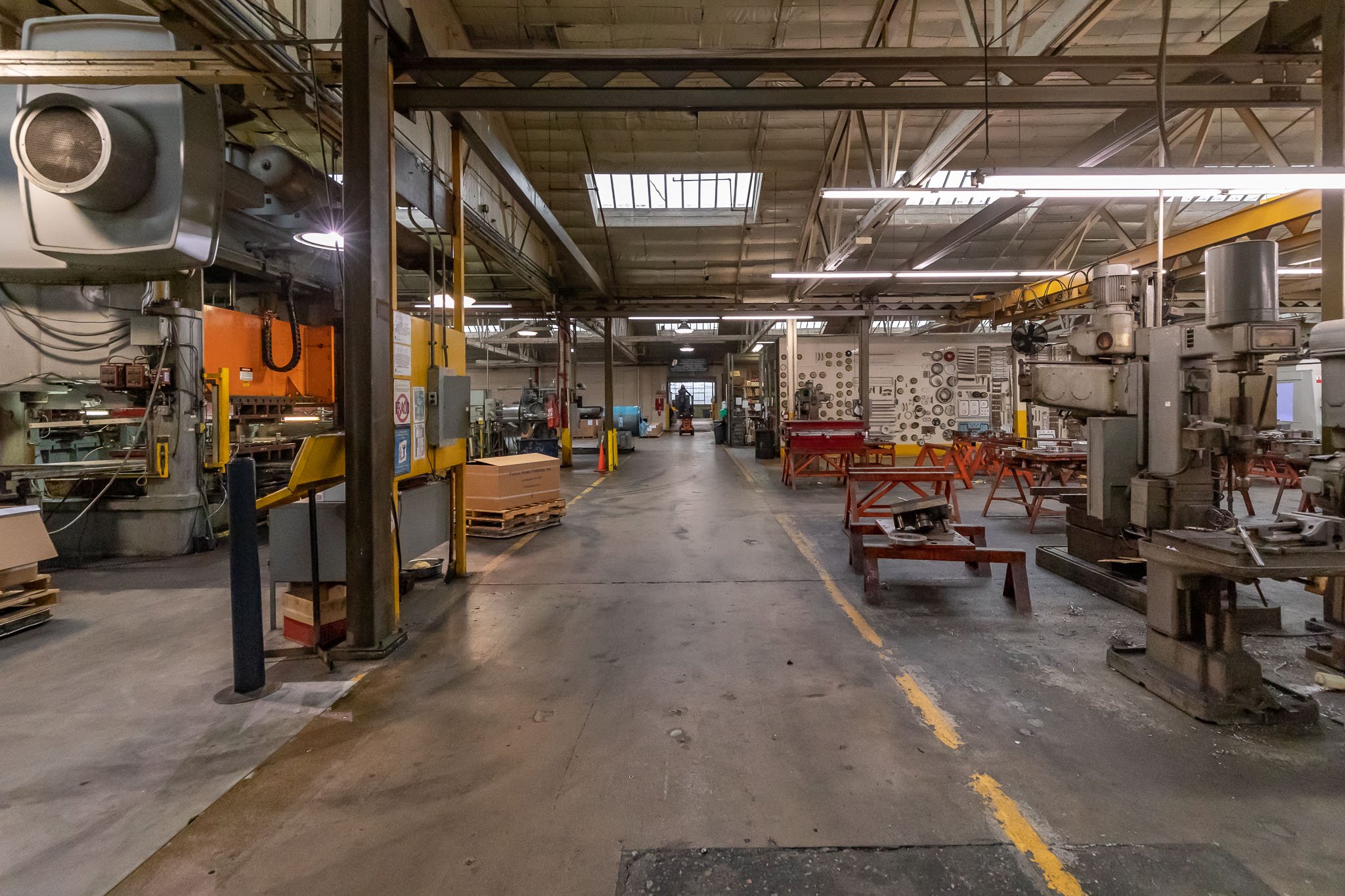 Empty industrial manufacturing workshop with machinery, workbenches, and safety cones, viewed from the entrance with an open space in the center.