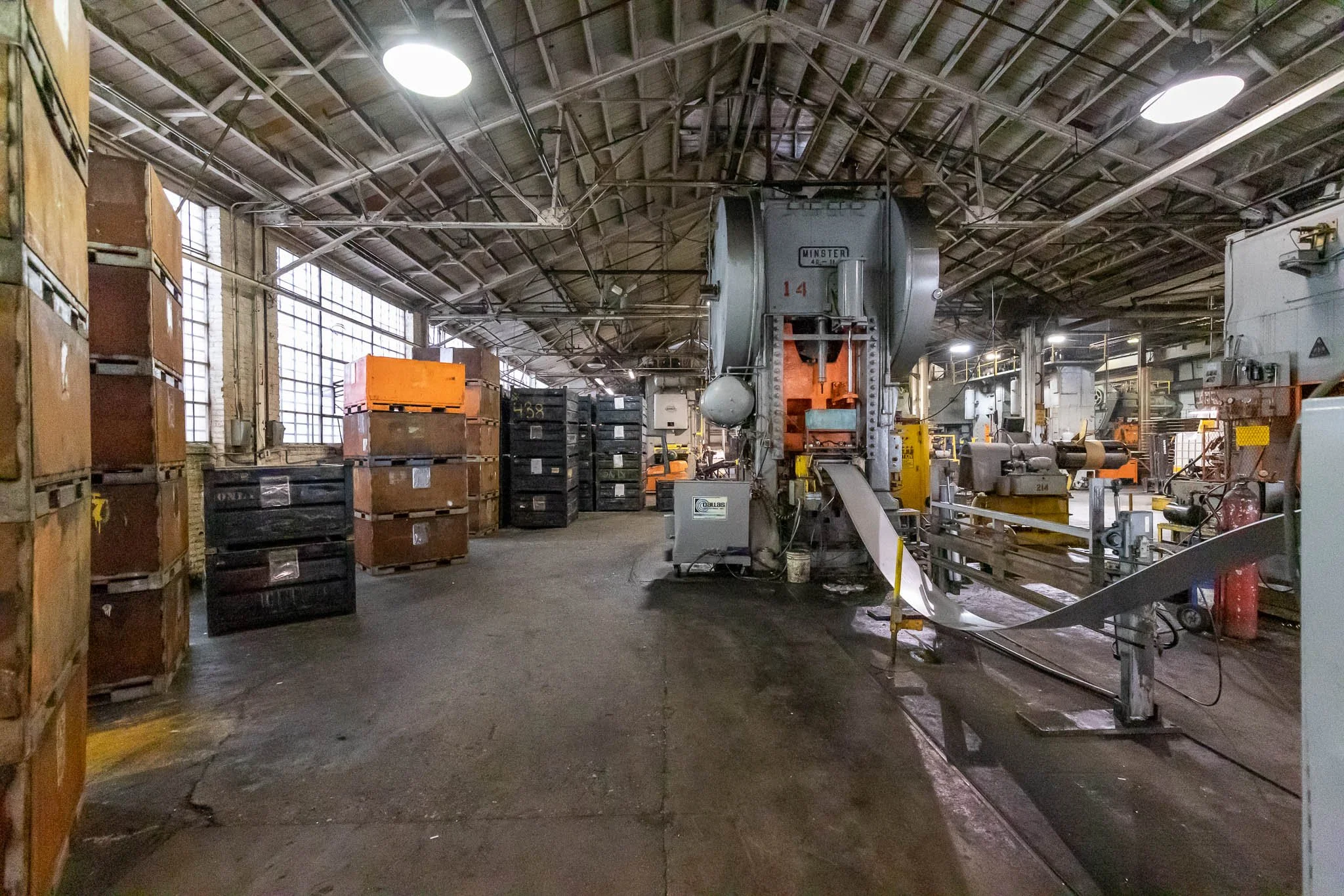 Industrial factory interior with large machinery, stacked crates, and overhead lighting.
