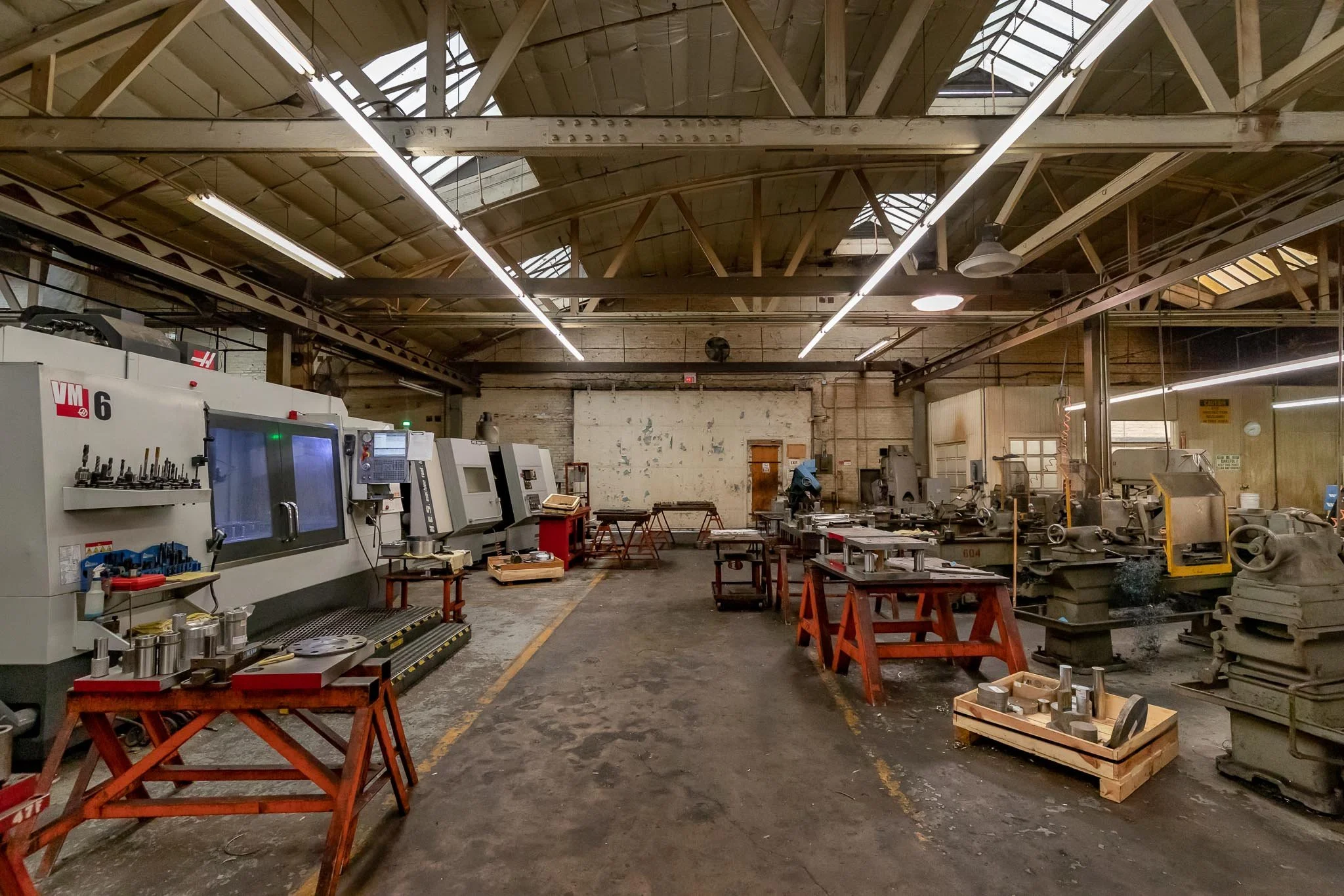 Industrial workshop with CNC machines, workbenches, and metalworking tools in a spacious, well-lit factory.