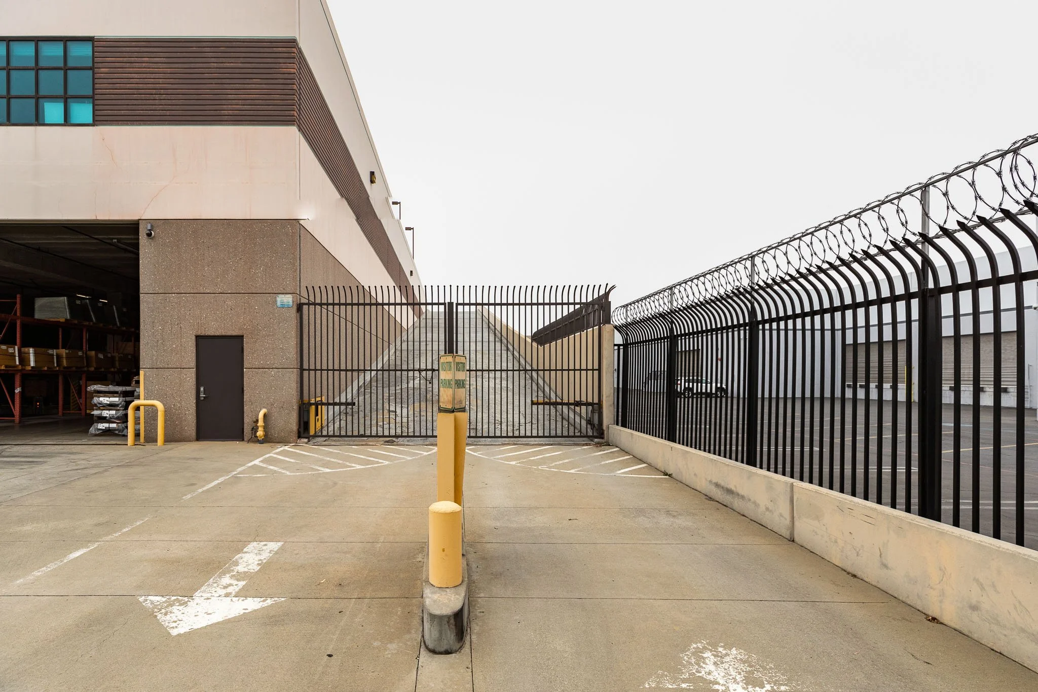 Empty parking lot with a locked gate, concrete pavement, and a building with a parking garage entrance on the left.