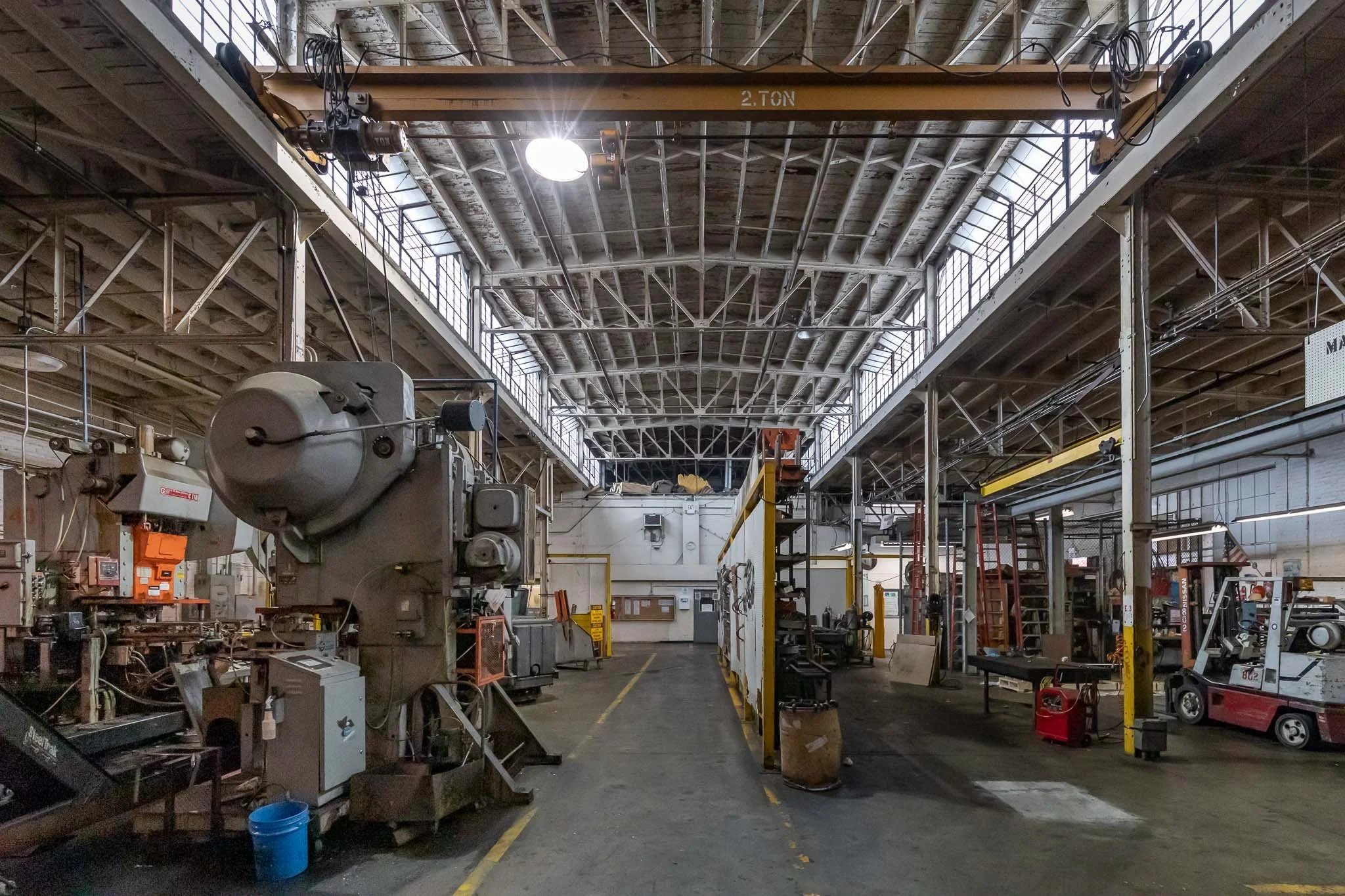 Industrial warehouse interior with machinery, tools, and equipment, high ceilings with skylights, and an overhead crane labeled '2. TON'.