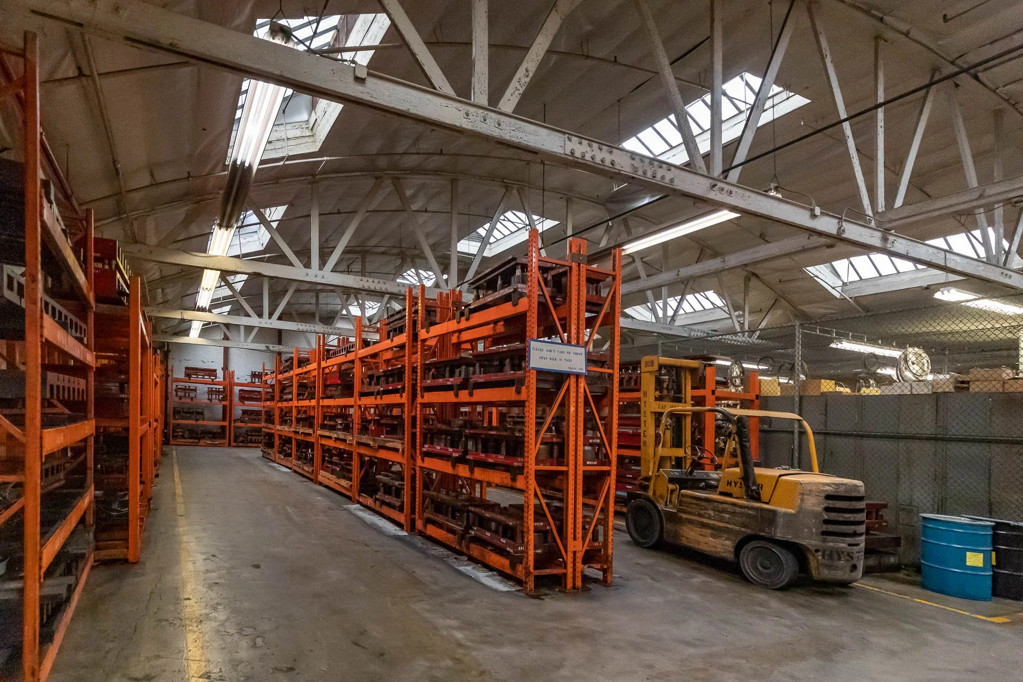 Warehouse interior with orange metal shelving units holding various items and a forklift parked beside them.