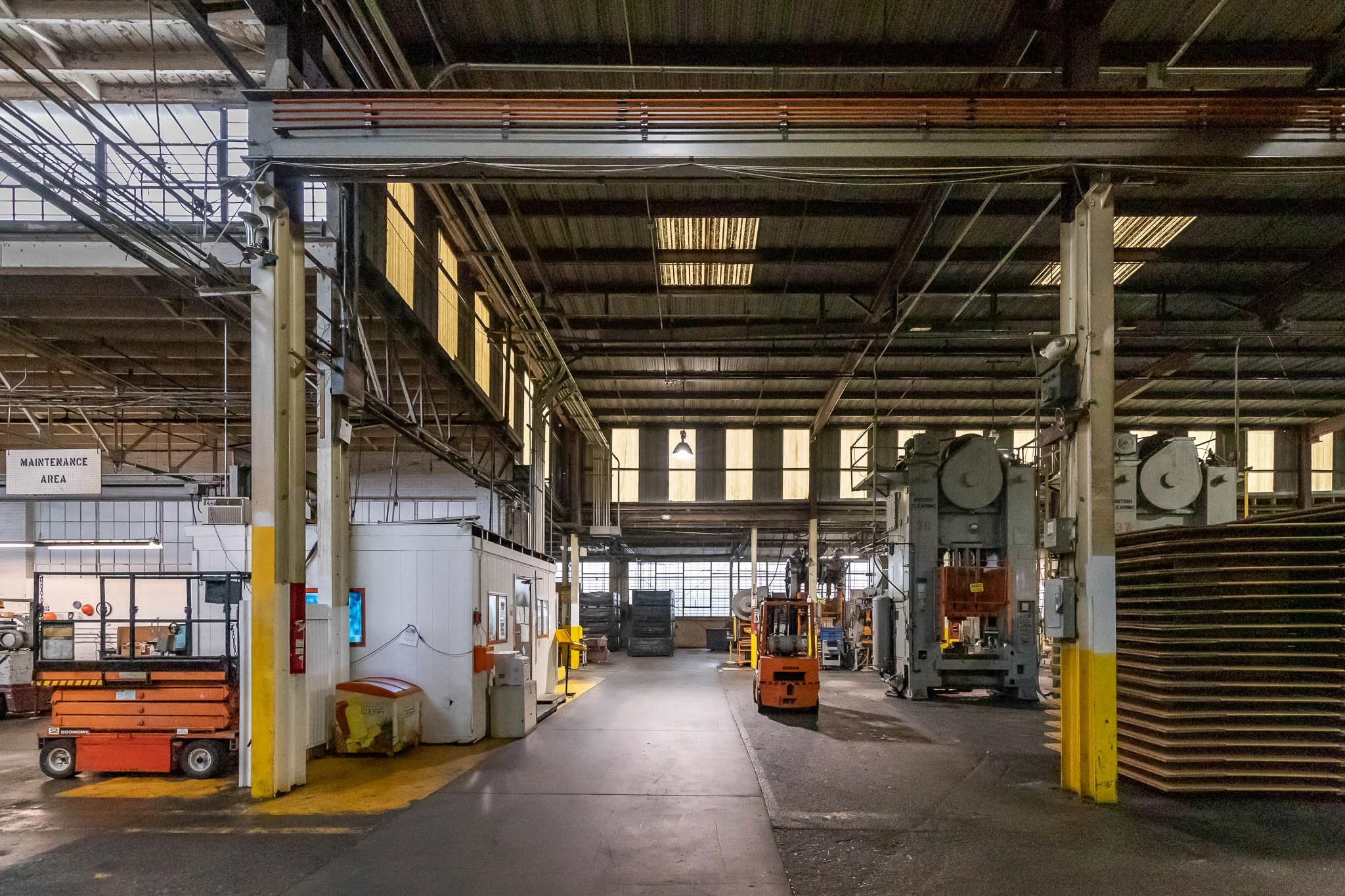 Industrial warehouse with machinery, equipment, and pallets, illuminated by natural light coming through the windows.