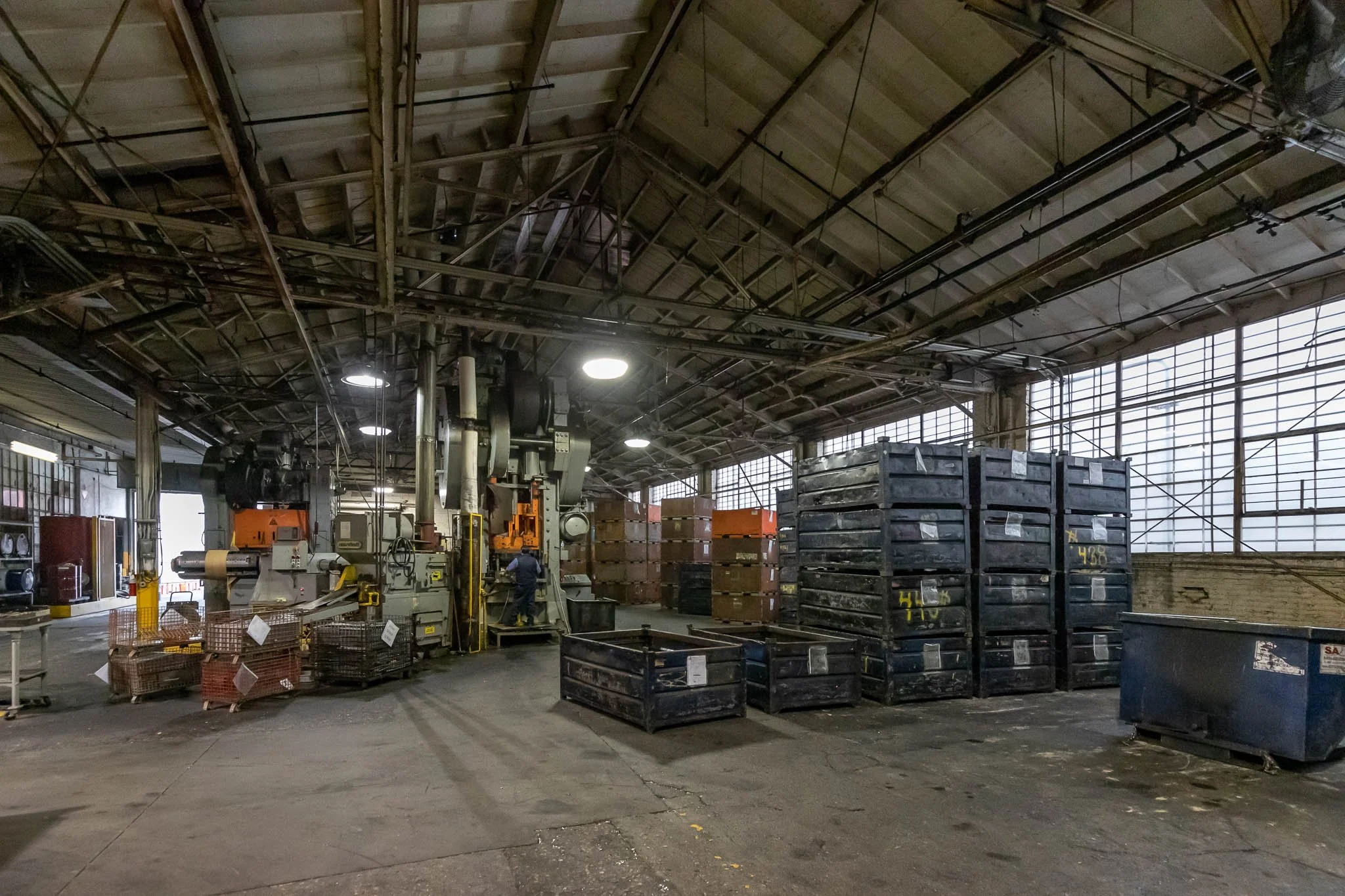 Industrial warehouse interior with large machinery, stacked crates, and a worker operating equipment