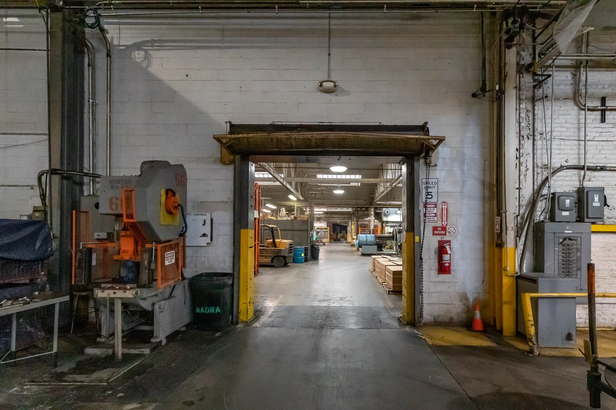 View through an industrial warehouse doorway showing machines, tools, and supplies inside.