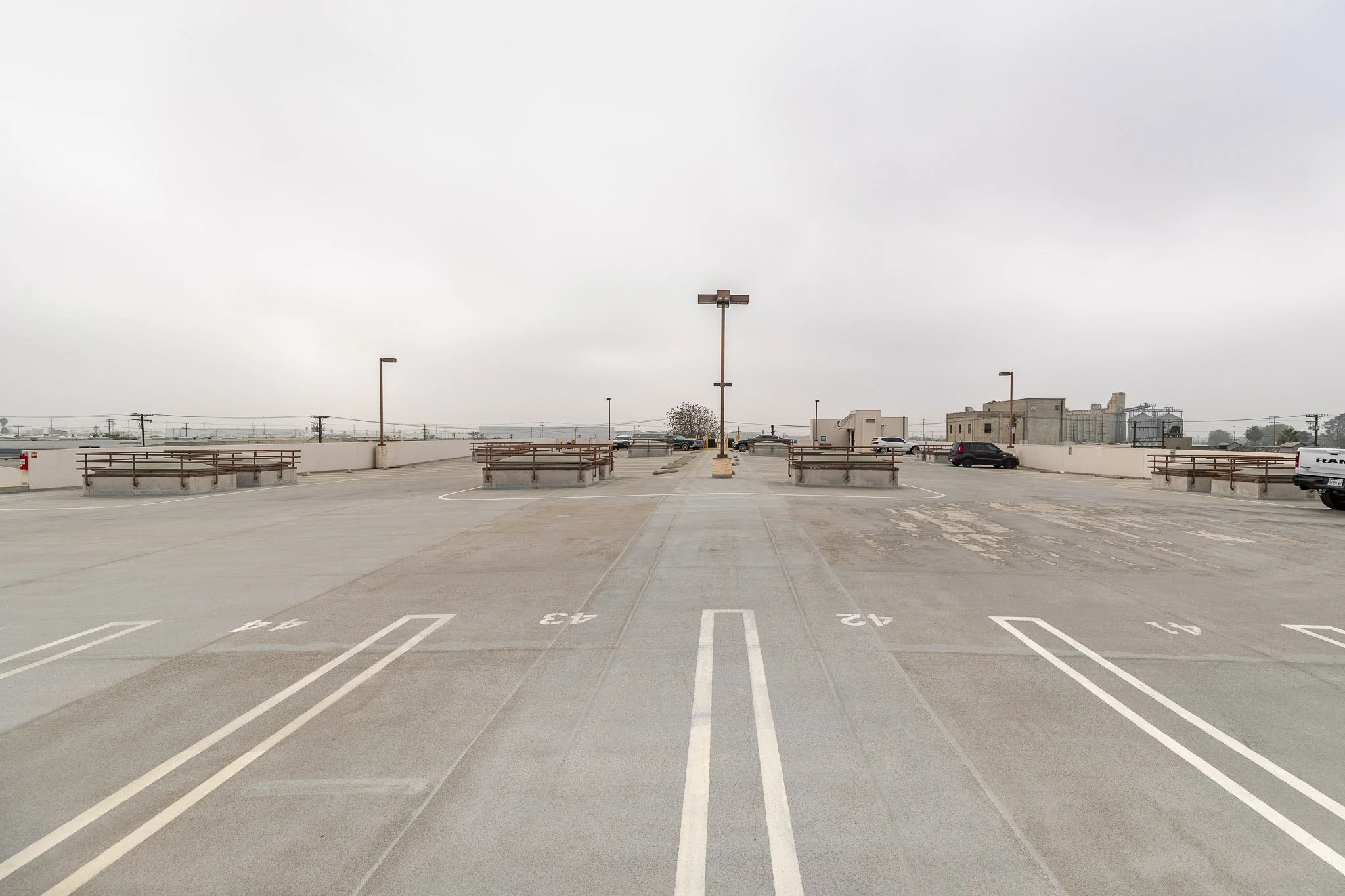 Empty rooftop parking lot with marked parking spaces, some cars parked, and a cloudy sky.