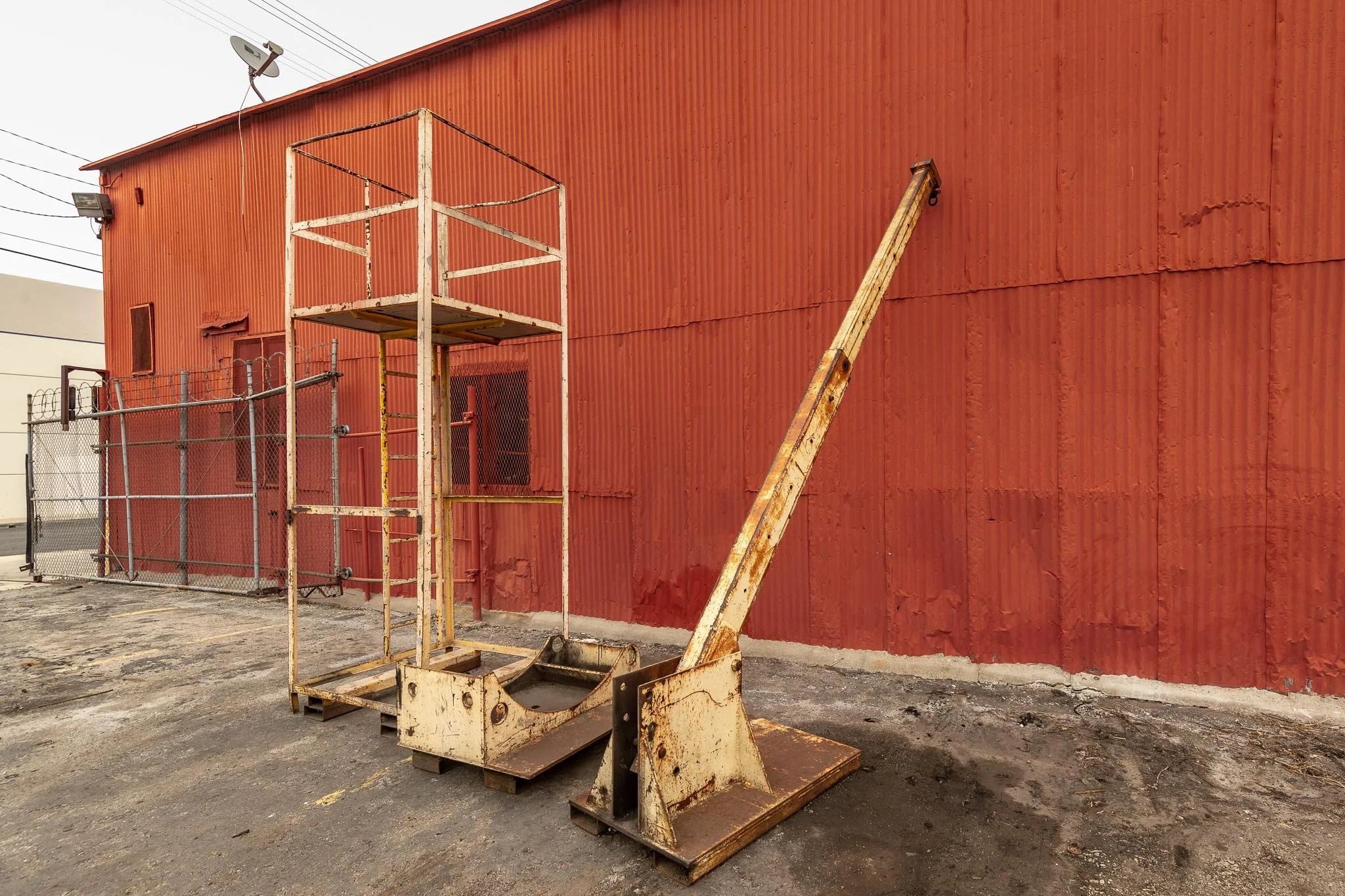 Old rusty construction lift with a platform next to a red corrugated metal building.
