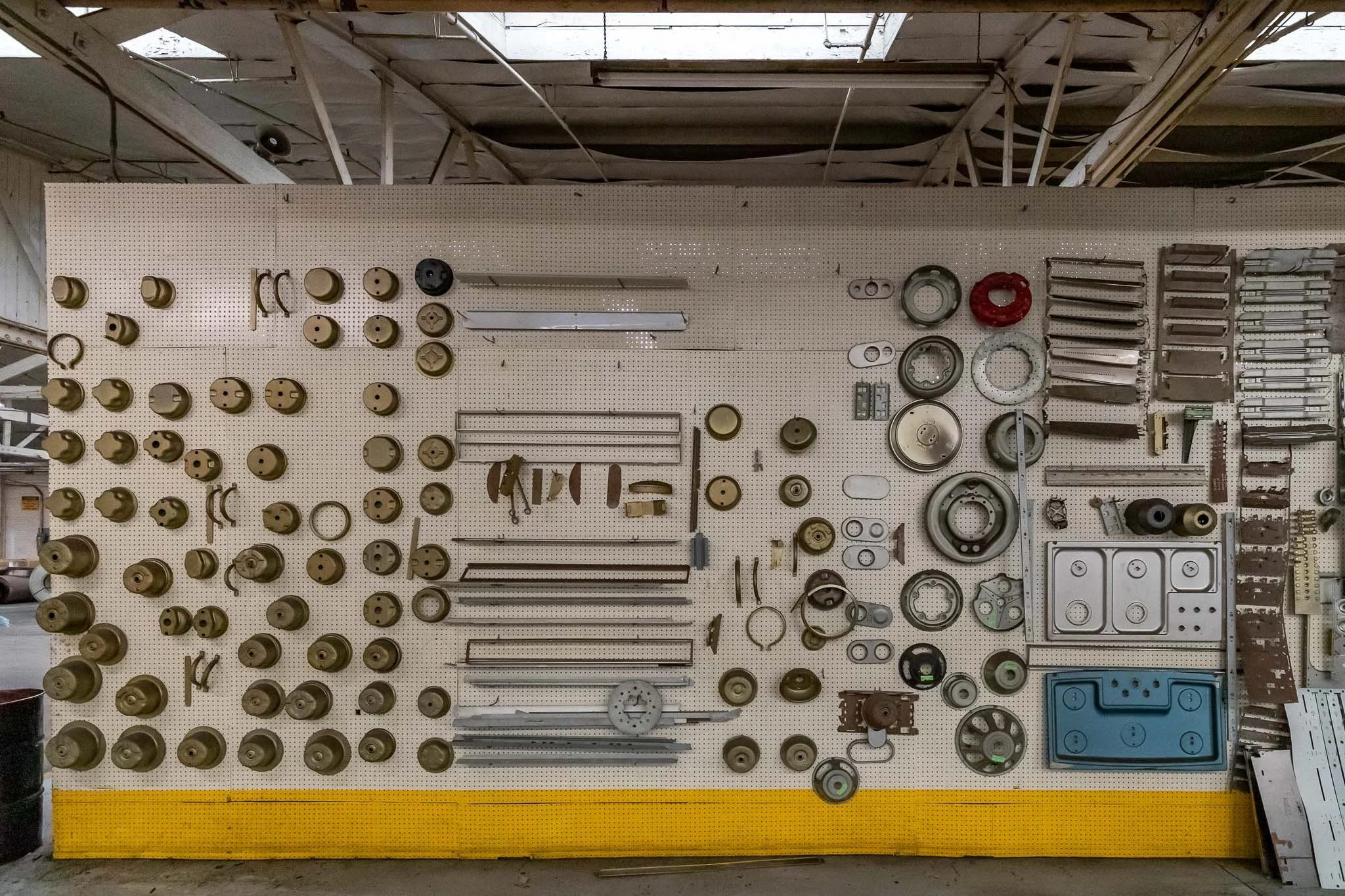 Pegboard wall with various metal and plastic mechanical parts and tools arranged in rows.