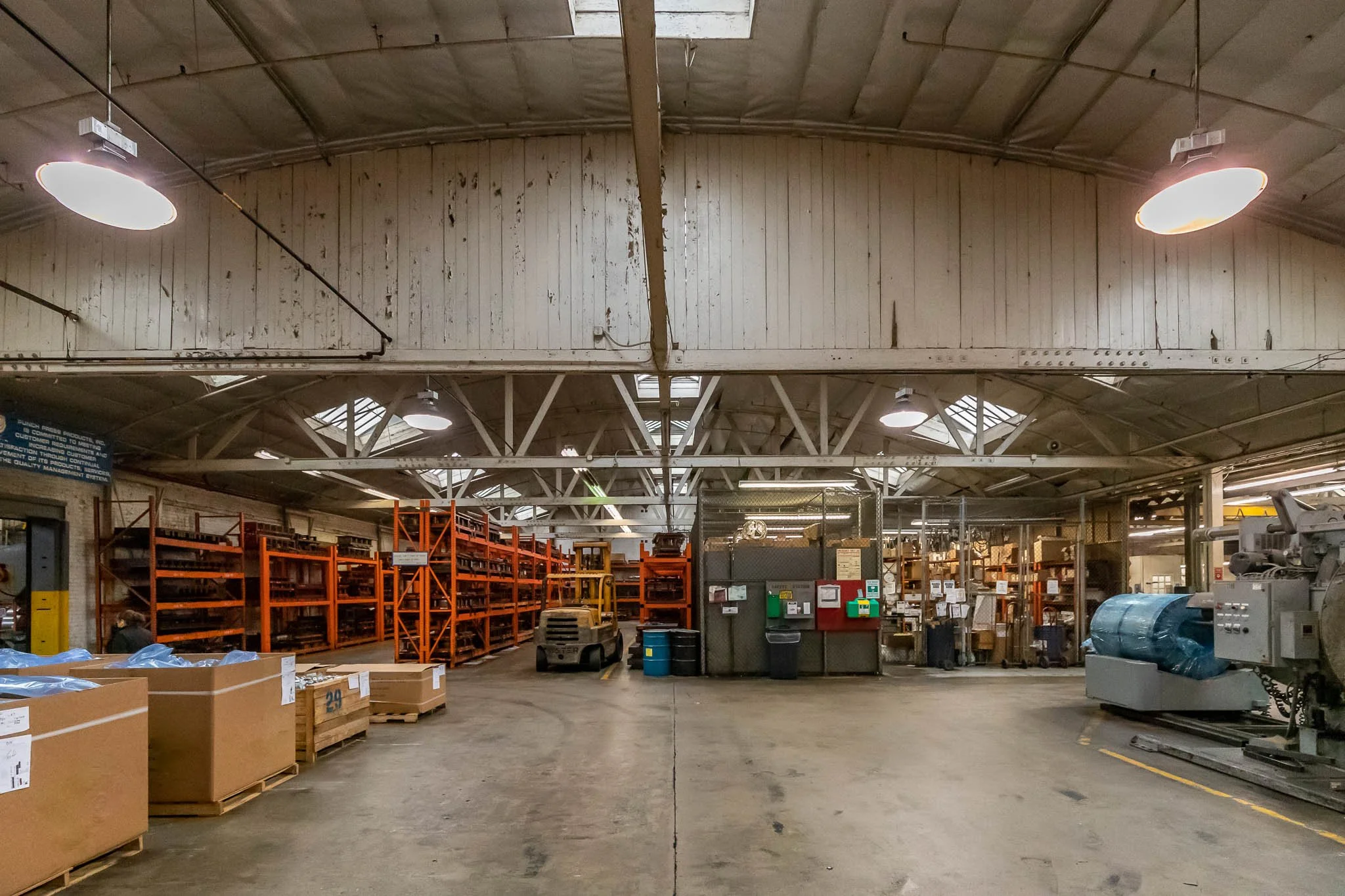 Interior of a warehouse with orange shelving units filled with boxes, a yellow fork lift, and various equipment and supplies.