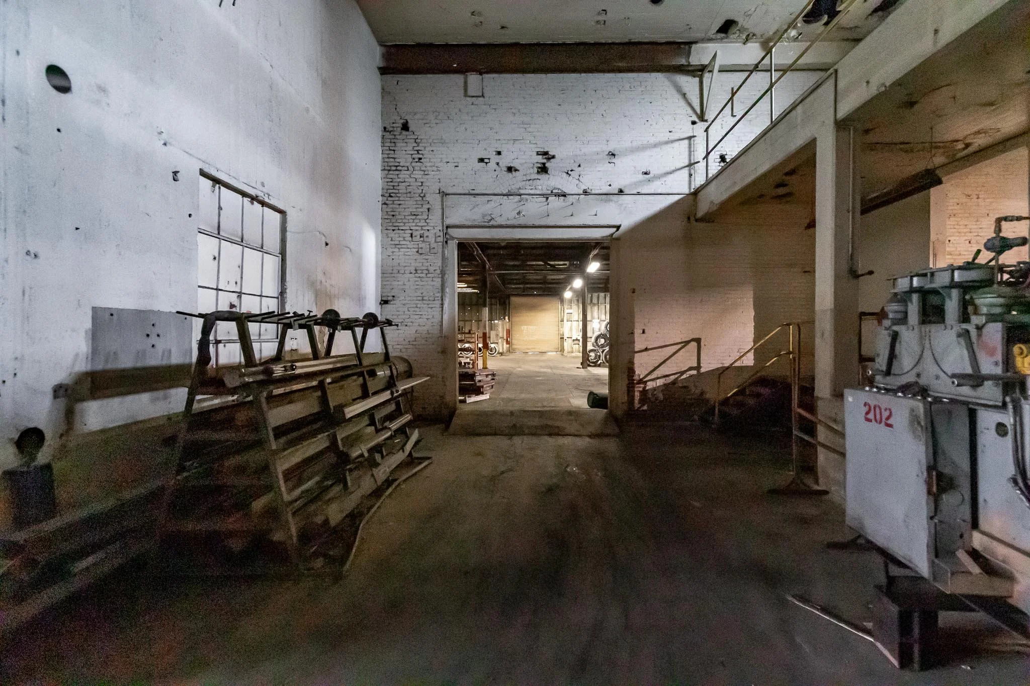 Interior of an abandoned industrial space with exposed brick and concrete walls, scattered equipment, and a distant open area.