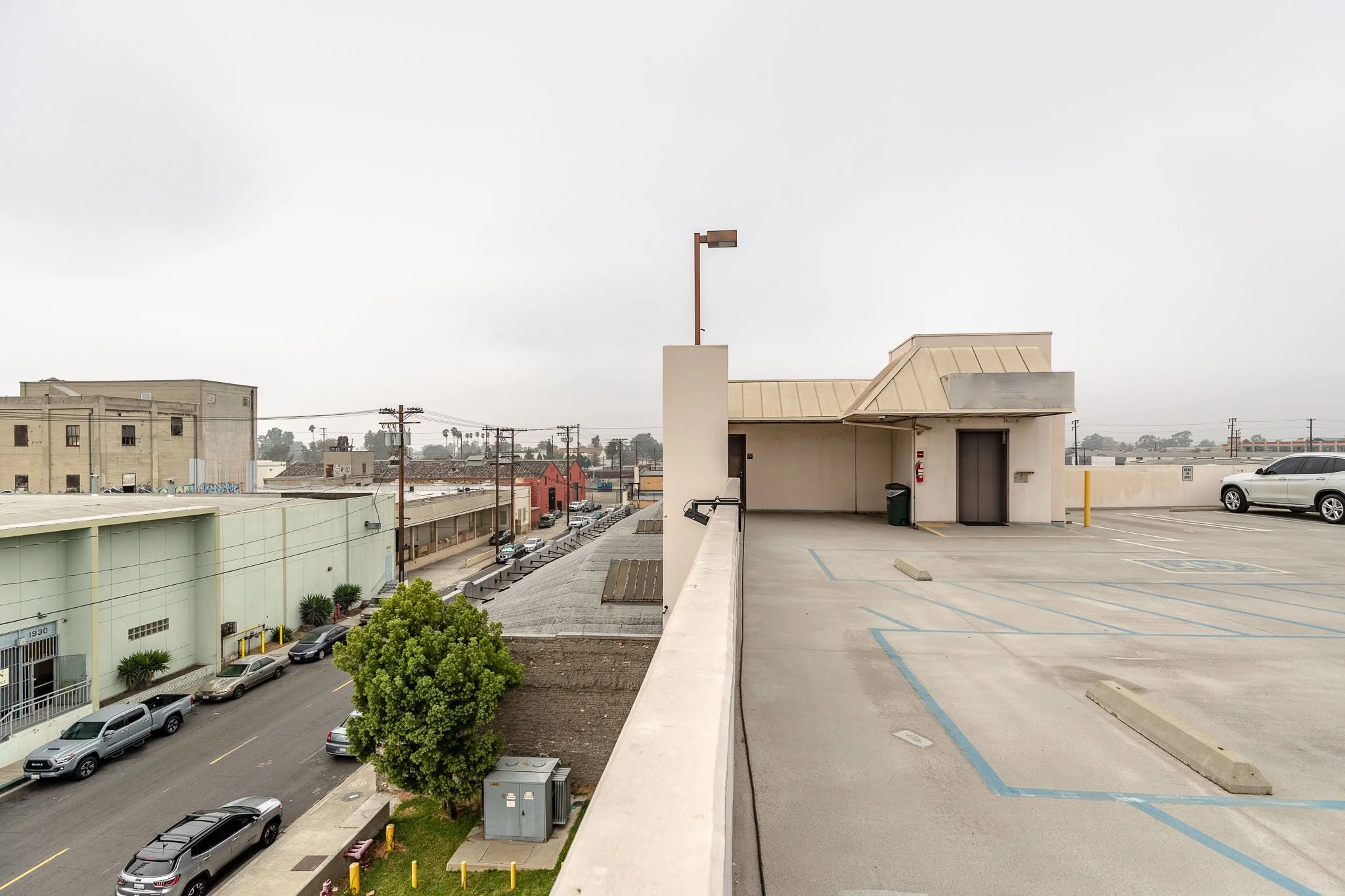 A split view of a city scene with the left side showing a street with parked cars and buildings, and the right side showing an empty parking lot with a building, a few cars, and a cloudy sky.