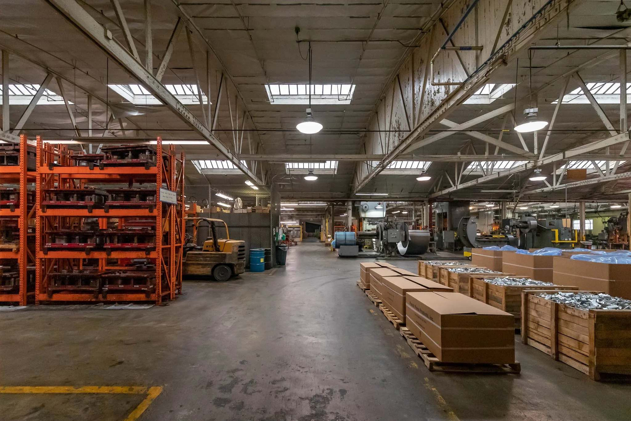 An industrial warehouse with shelves, machinery, forklift, and boxes on pallets.
