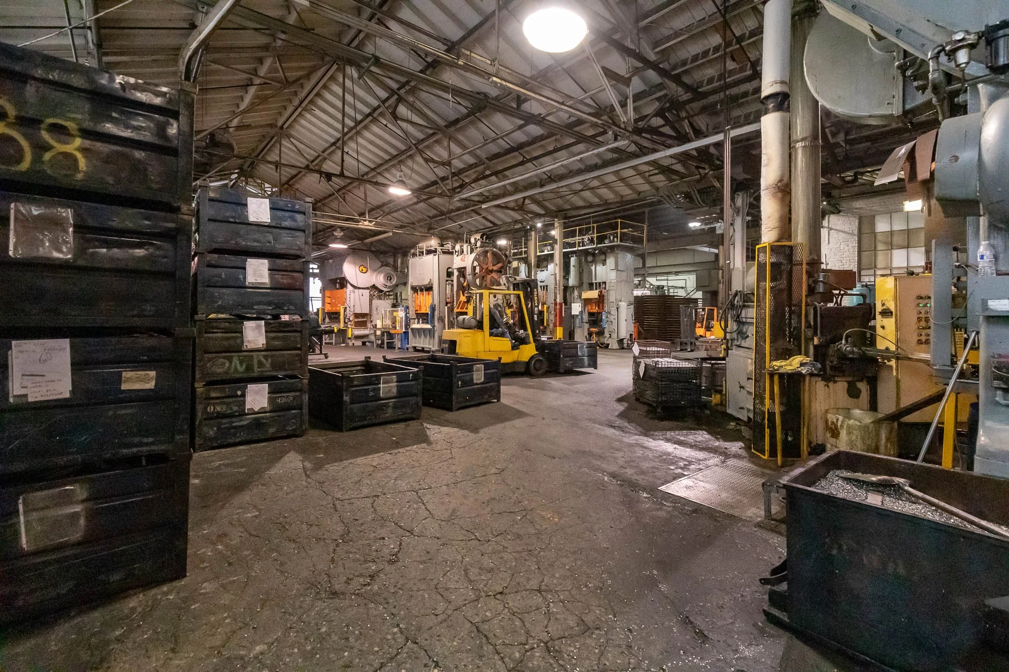 Interior of an industrial warehouse with stacked black crates, a yellow forklift, and various machinery.