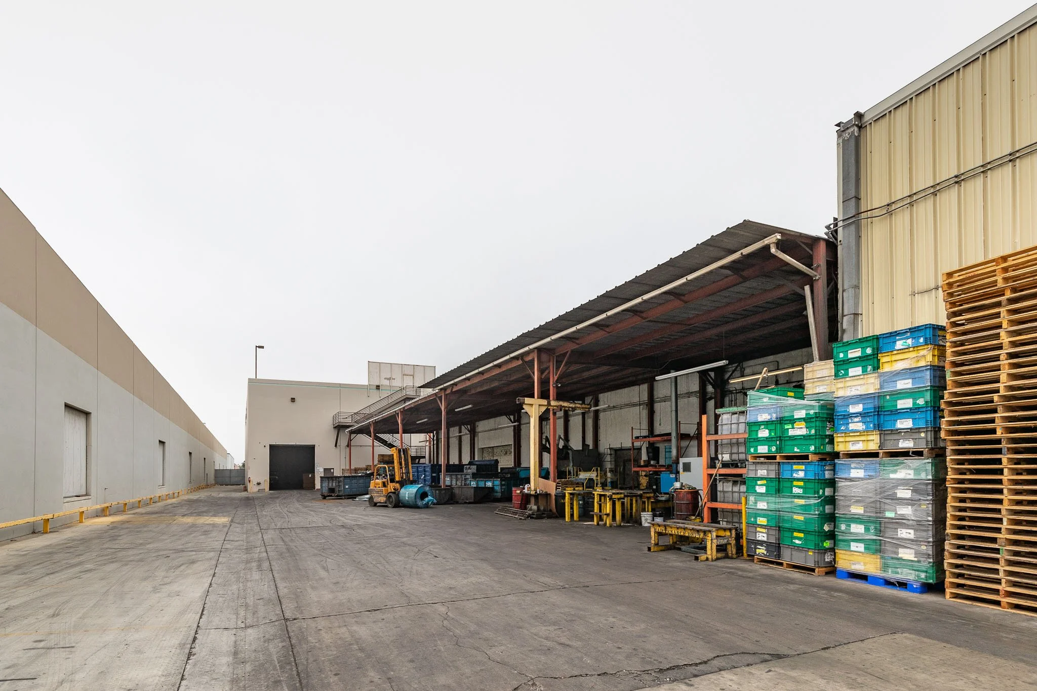 An outdoor industrial warehouse area with pallets, storage containers, and a forklift.