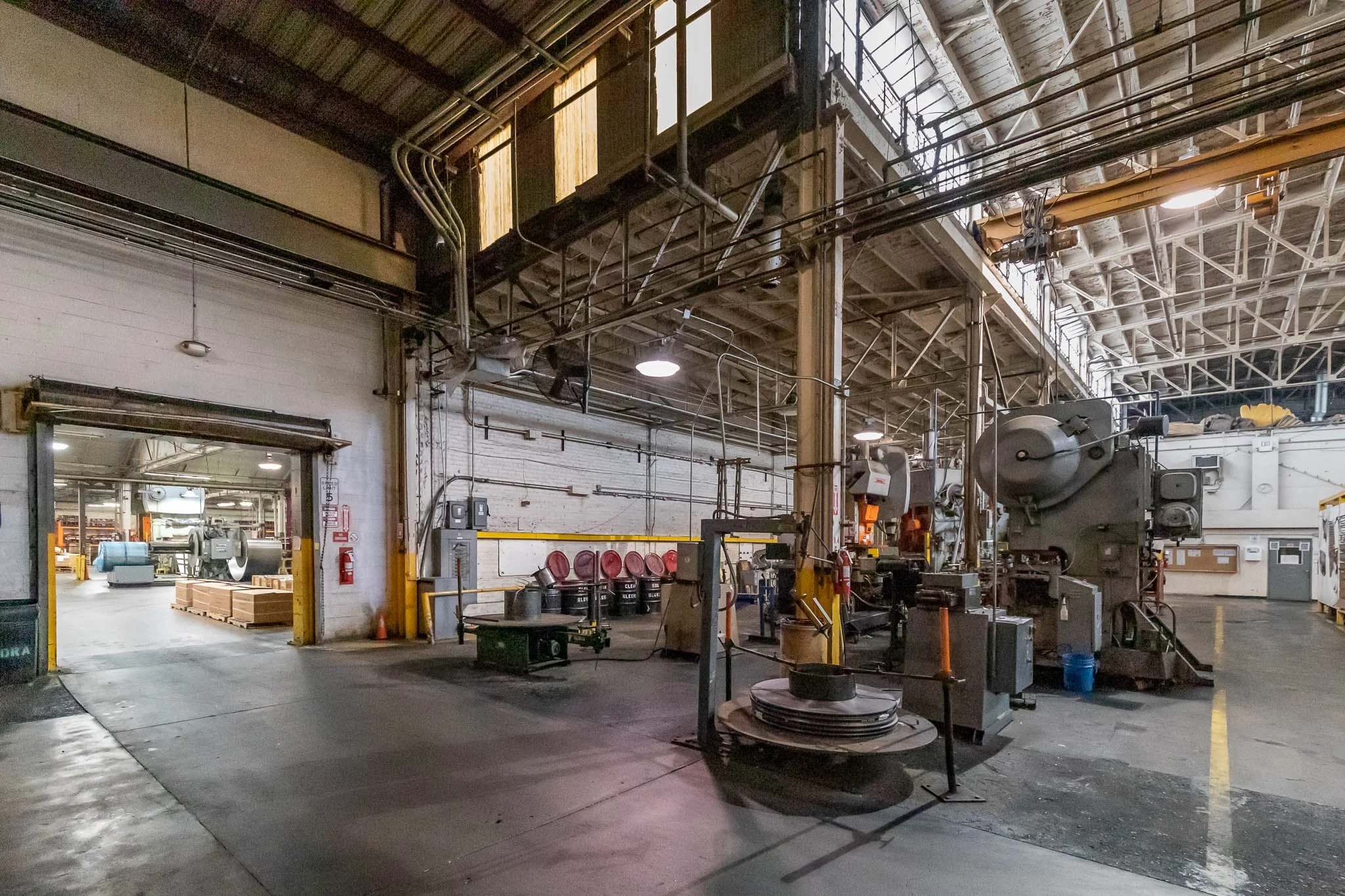 Interior of an industrial factory or warehouse with machinery, pipes, and storage areas.