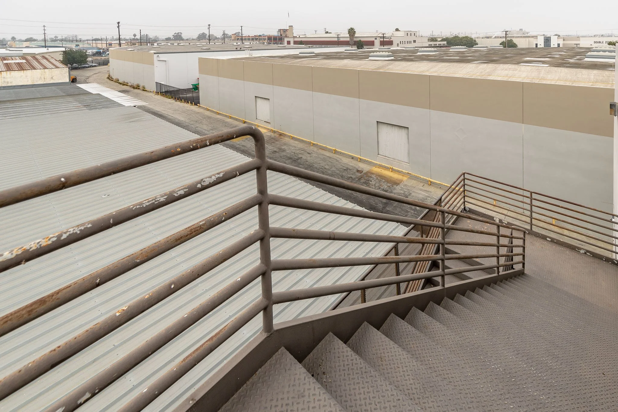 Industrial building exterior with metal staircase leading down to a roof and warehouse walls in the background.