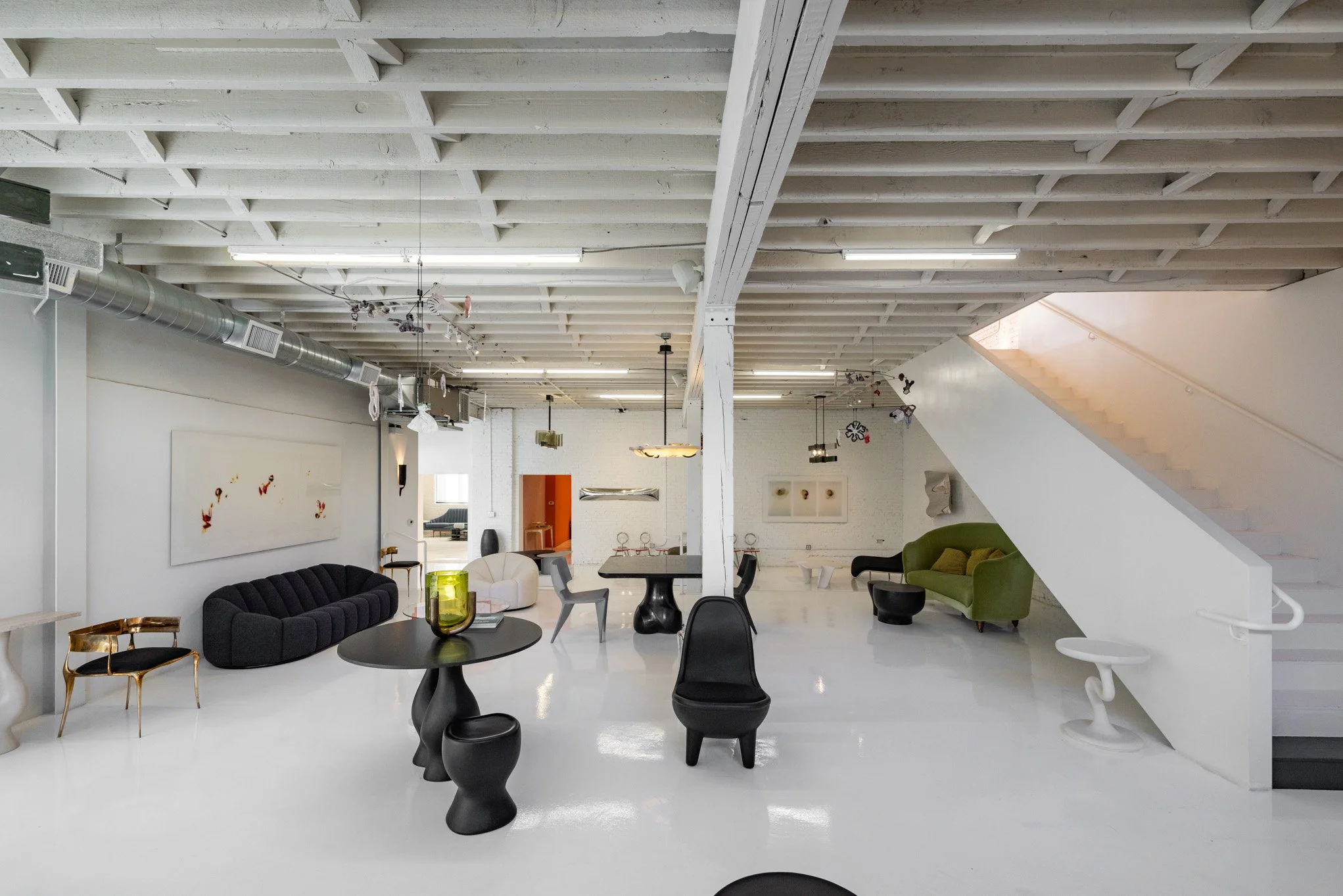 Modern, minimalist interior living space with white floors and ceiling, black and green furniture, and artistic decor.