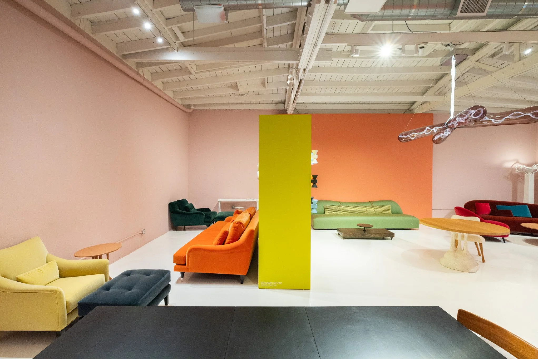 Colorful modern furniture arranged in a gallery space with pastel walls and exposed ceiling.