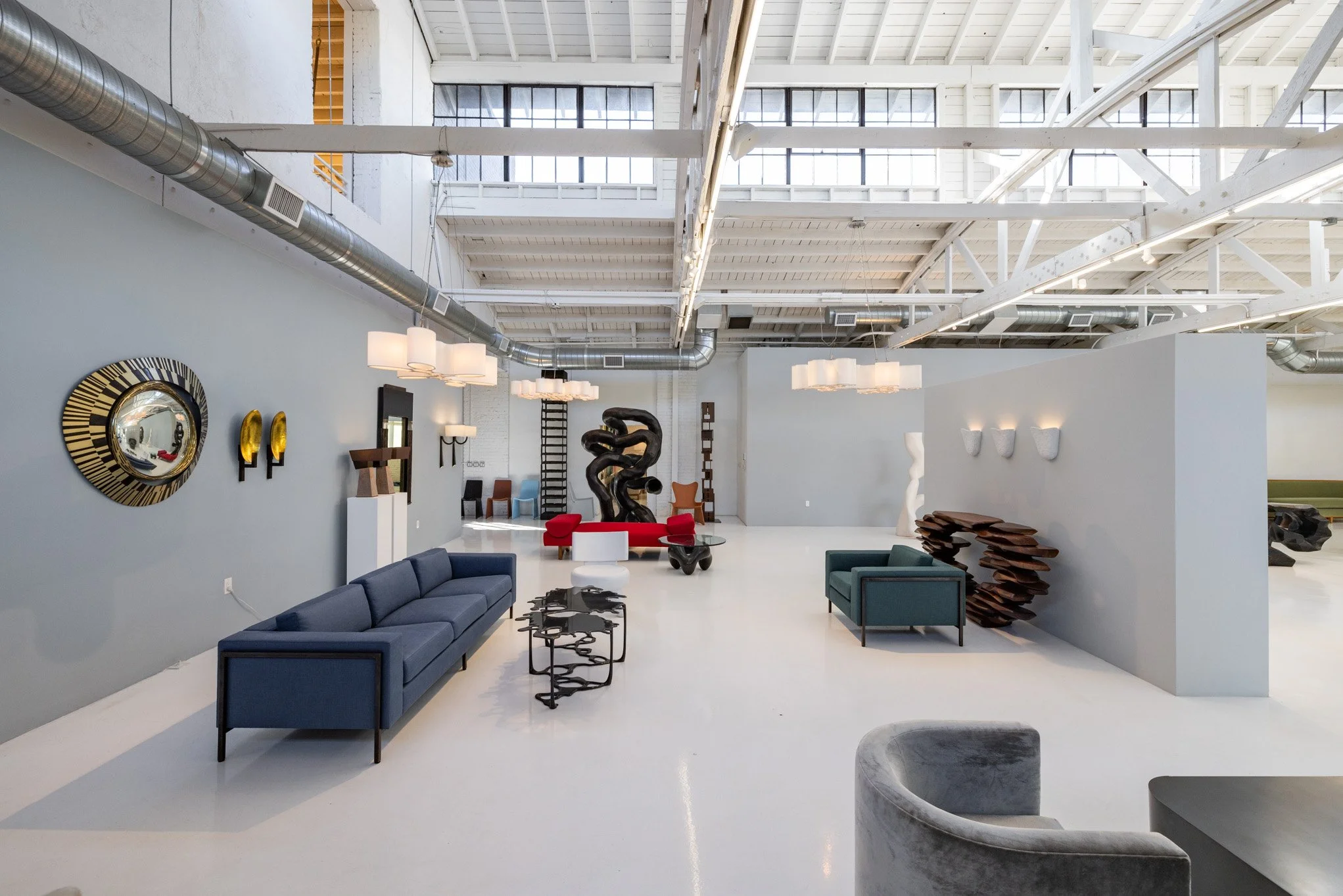 Interior of a modern art gallery with various sculptures and seating arrangements, high ceilings with visible beams and ductwork.