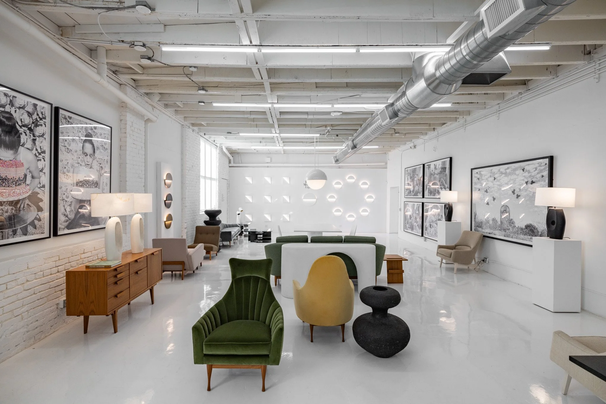 Modern art gallery with white walls, black and white photographs, contemporary chairs, and sculptures.