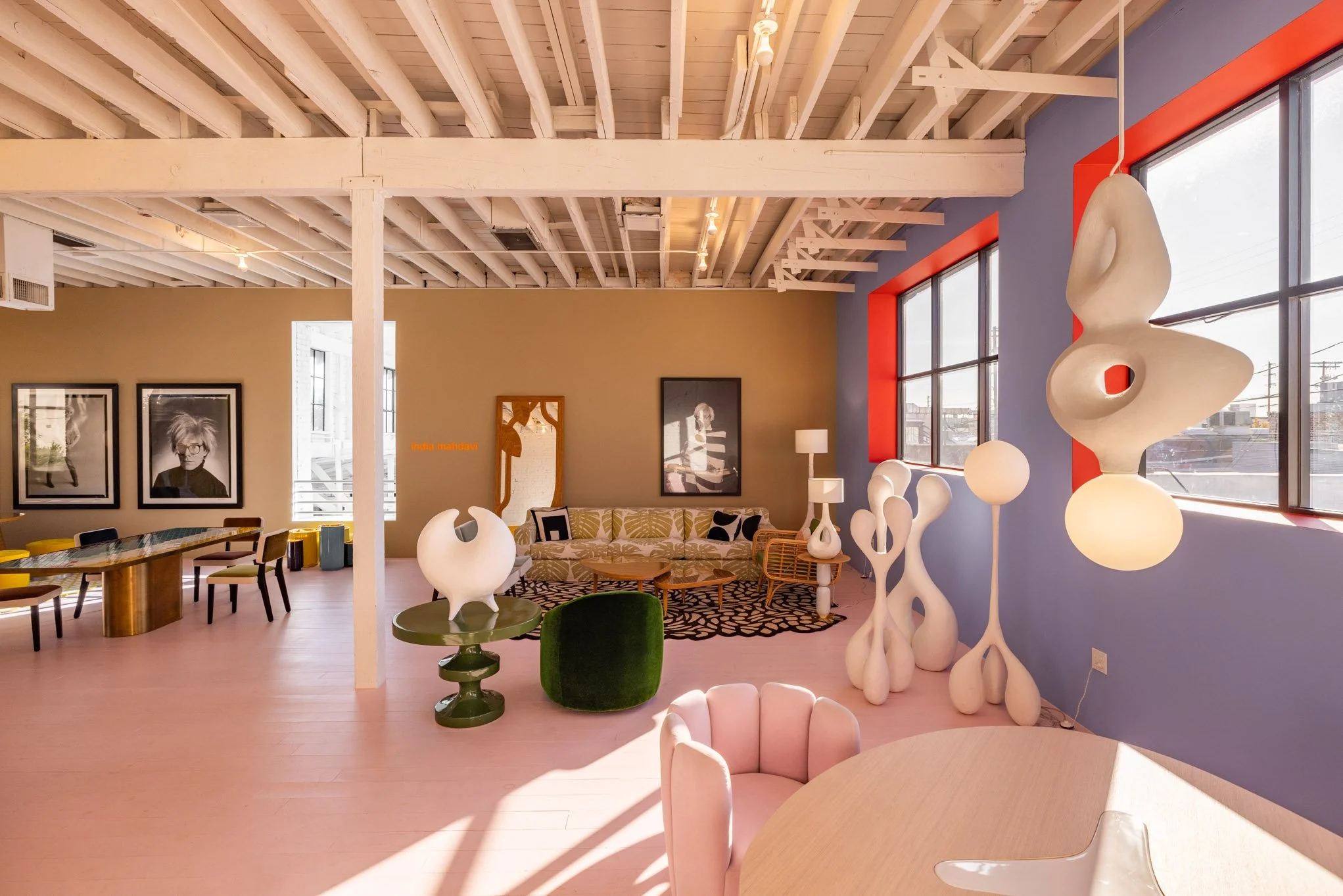 Modern living room with eclectic furniture, colorful walls, abstract sculptures, large windows, and artwork.