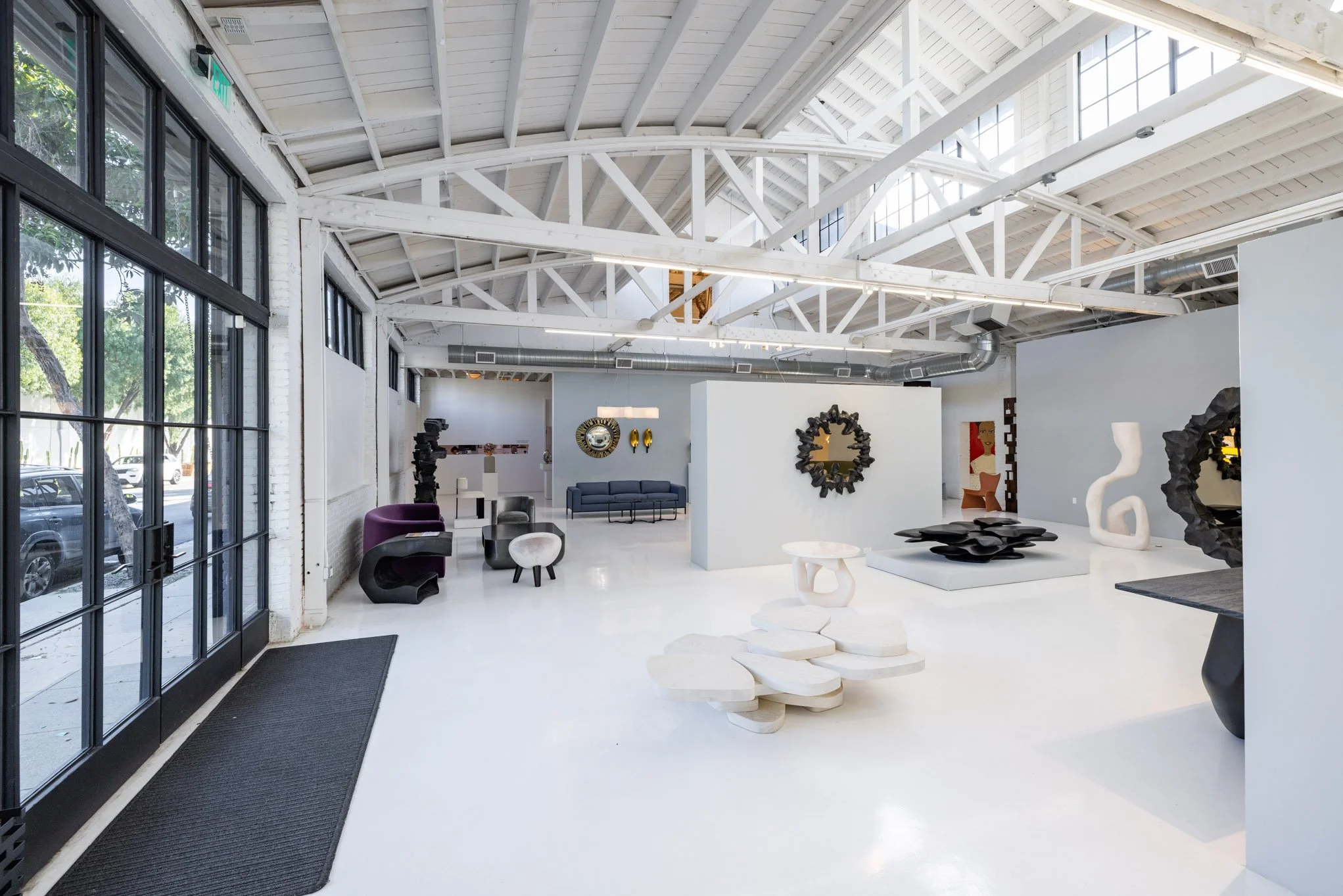 Interior of an art gallery with white walls, high ceiling with exposed beams, and various modern sculptures and wall art decor.