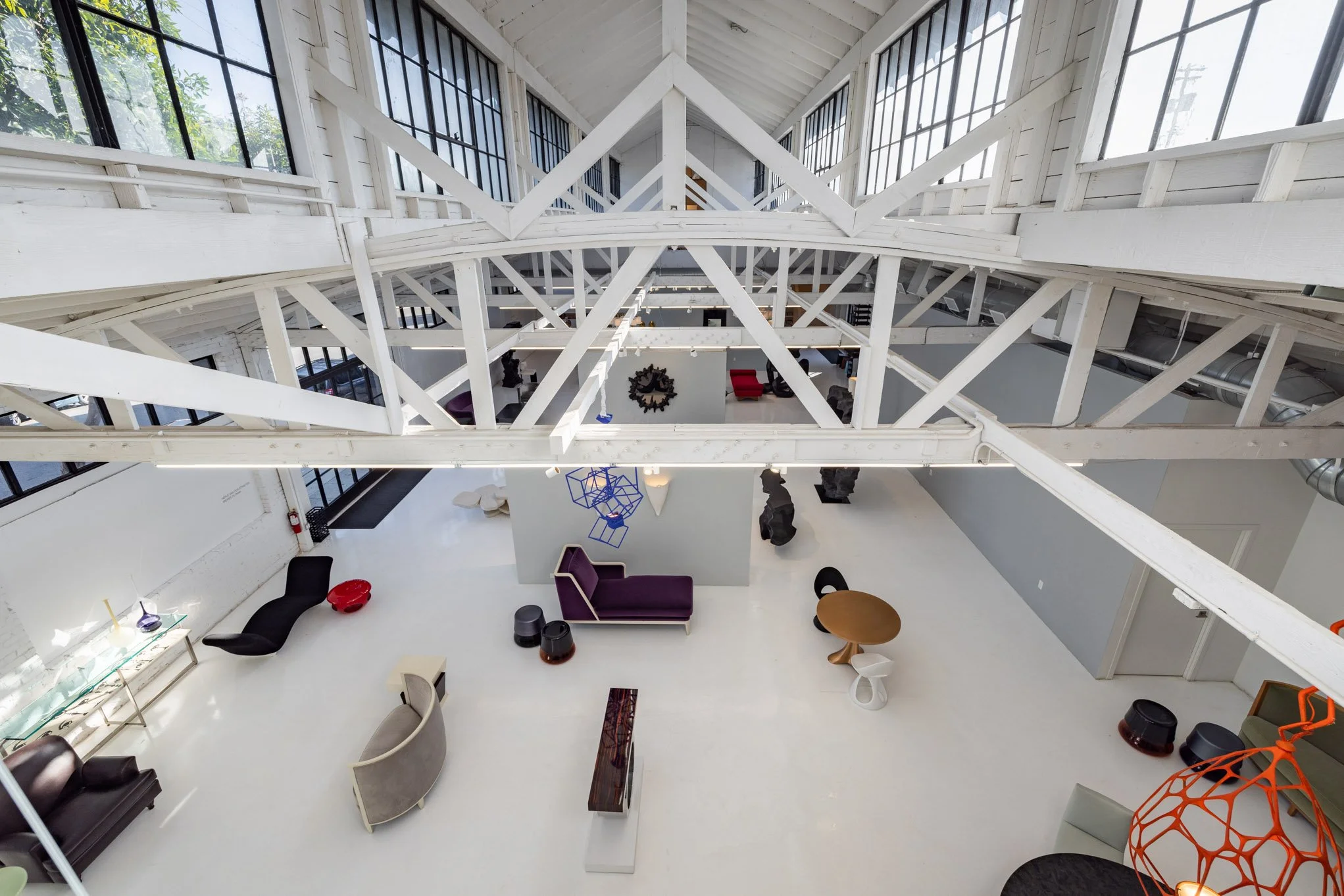 Interior view of a modern, industrial-style loft with exposed white beams, large windows, and various contemporary furniture pieces including chairs, tables, and sculptures.