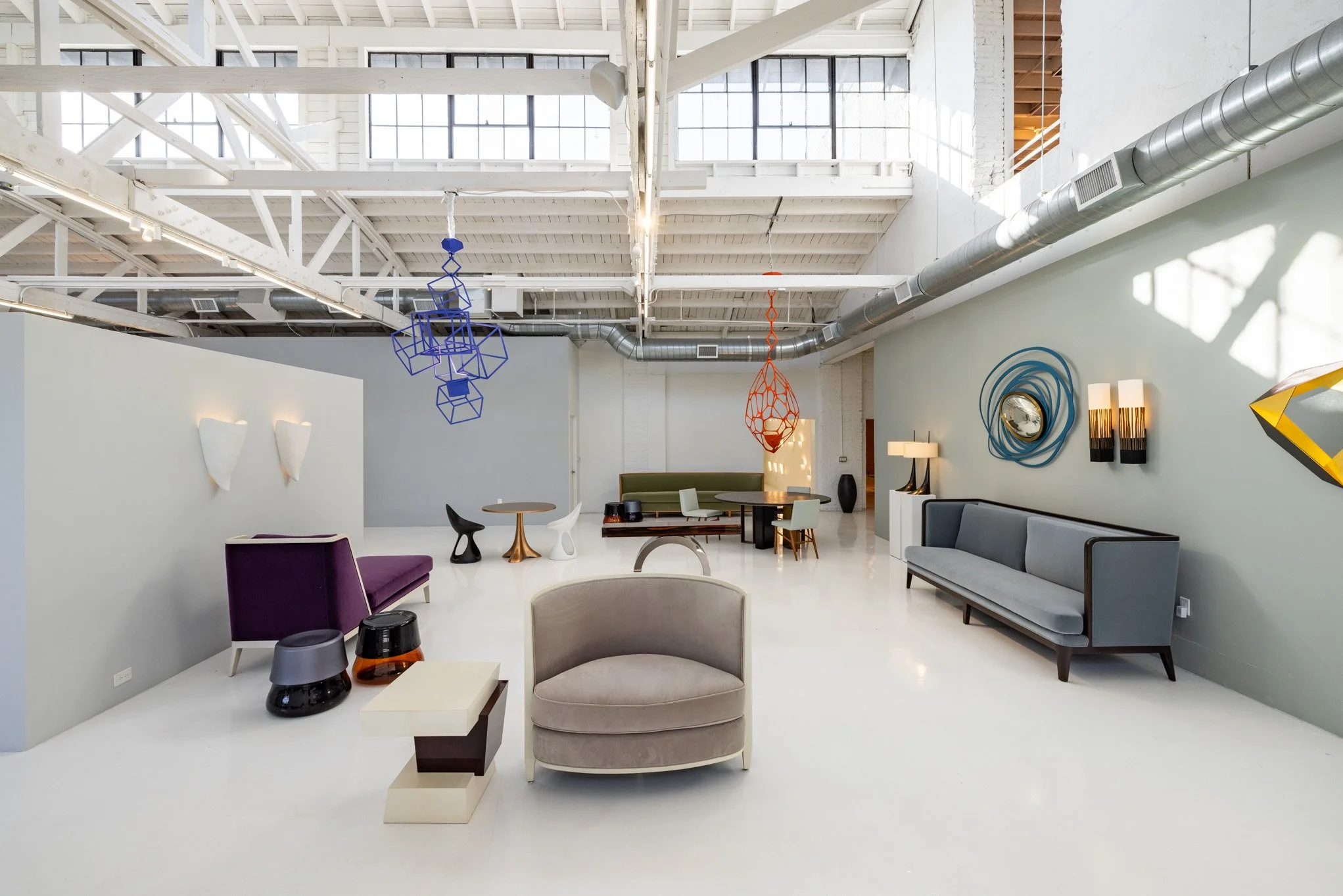 Modern, spacious interior with colorful hanging art pieces, contemporary sofas, and eclectic decor in an industrial-style space with high ceilings and large windows.