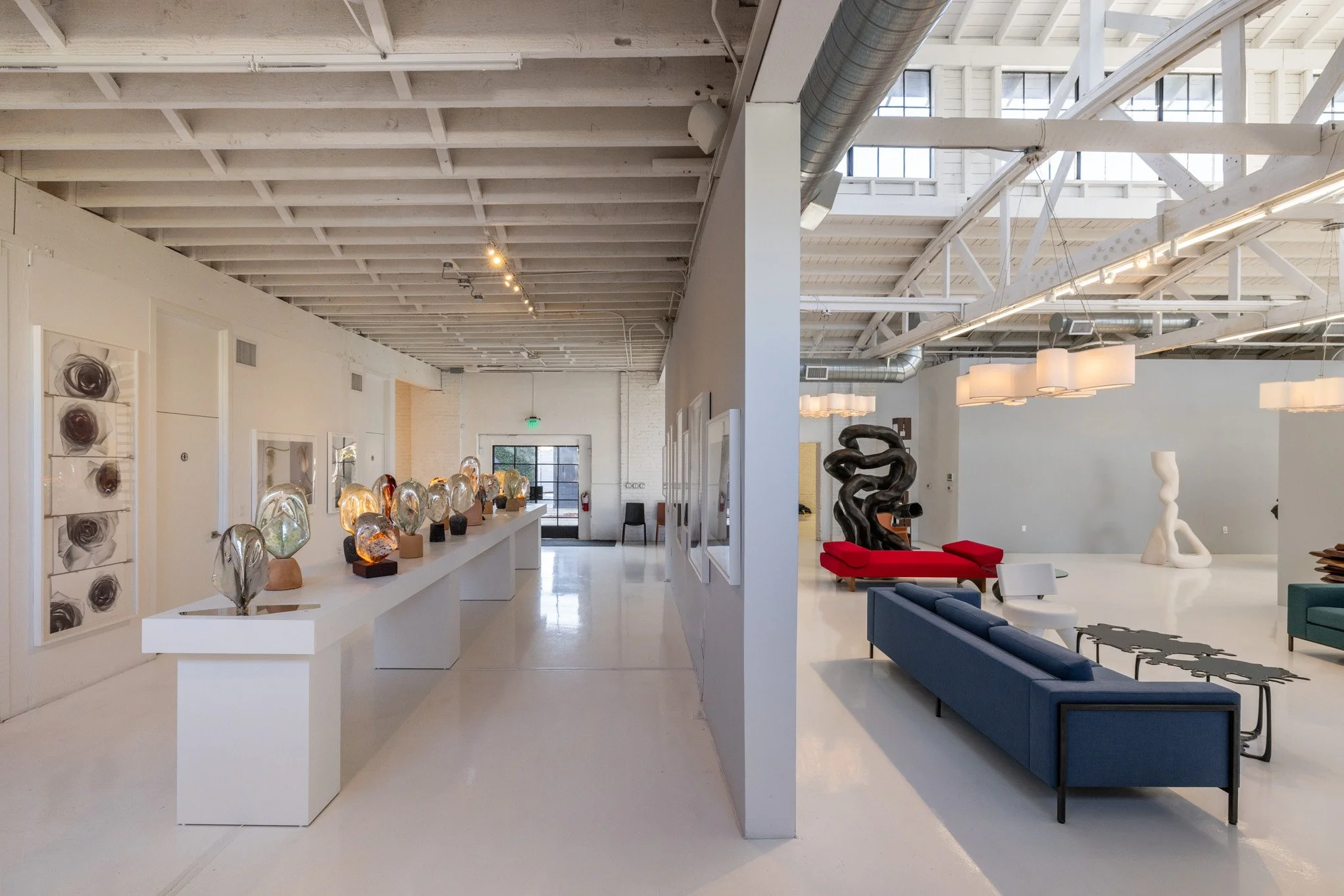 Interior of an art gallery with sculptures, paintings, and modern furniture, divided into two sections with different art displays.