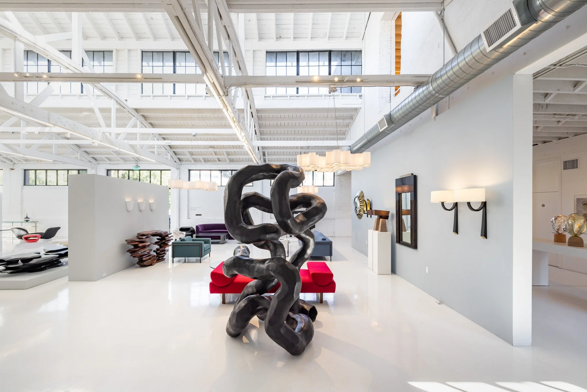 Modern art gallery interior with abstract black sculpture, colorful seating, and various art pieces on display.