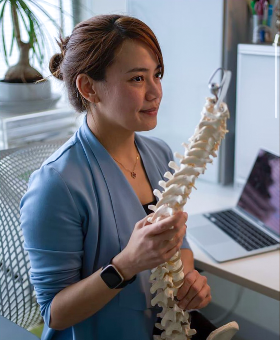 A woman in a blue blazer holding a model of a human spine in an office setting.