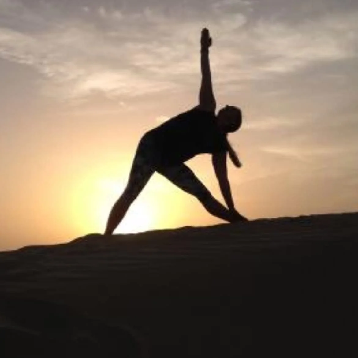 Silhouette of a person stretching or exercising on a hilltop at sunset with a partly cloudy sky.