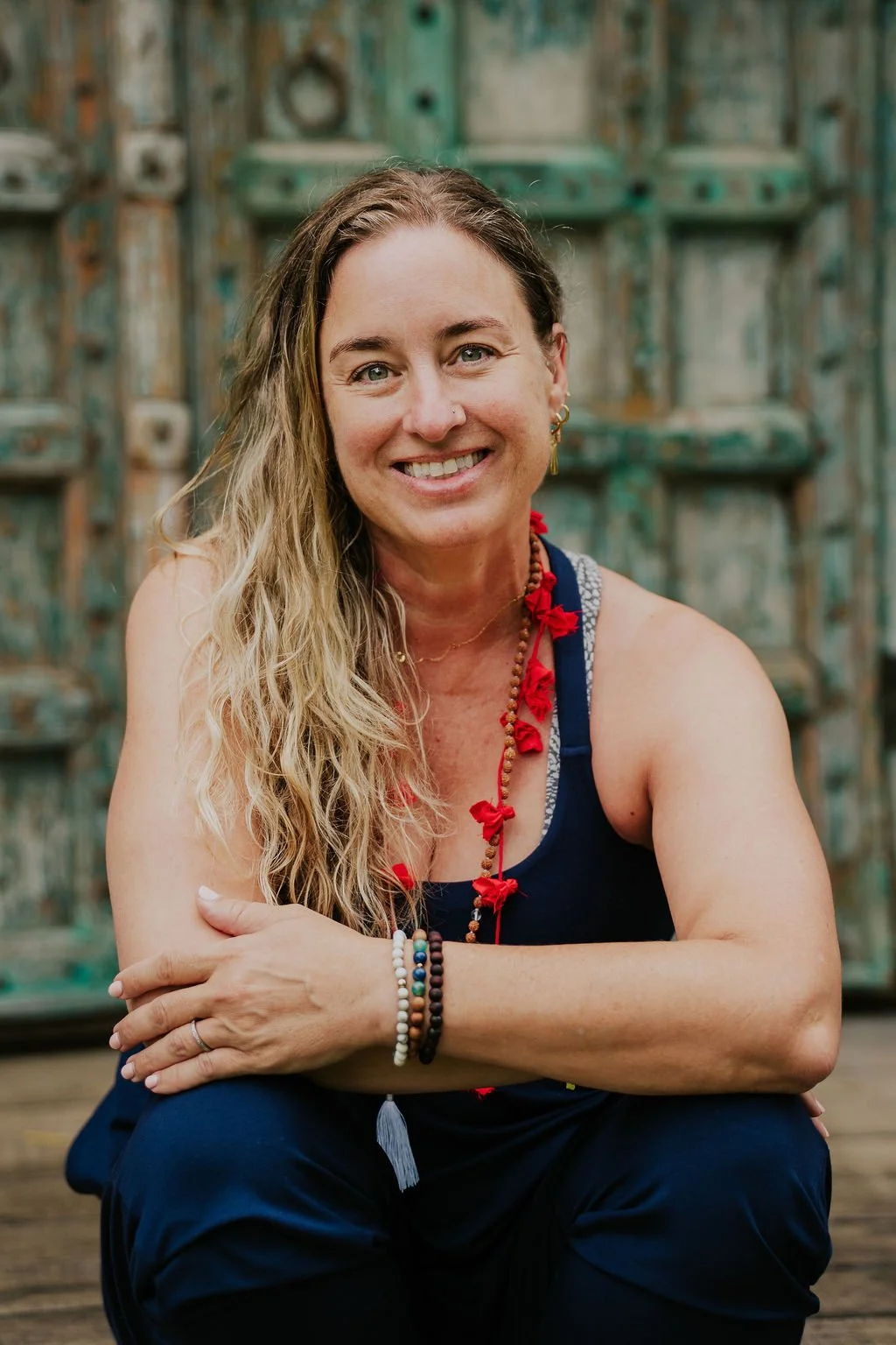 Casey Gill pictured seated after yoga practice with a friendly smile, arms crossed, and wearing mala beads