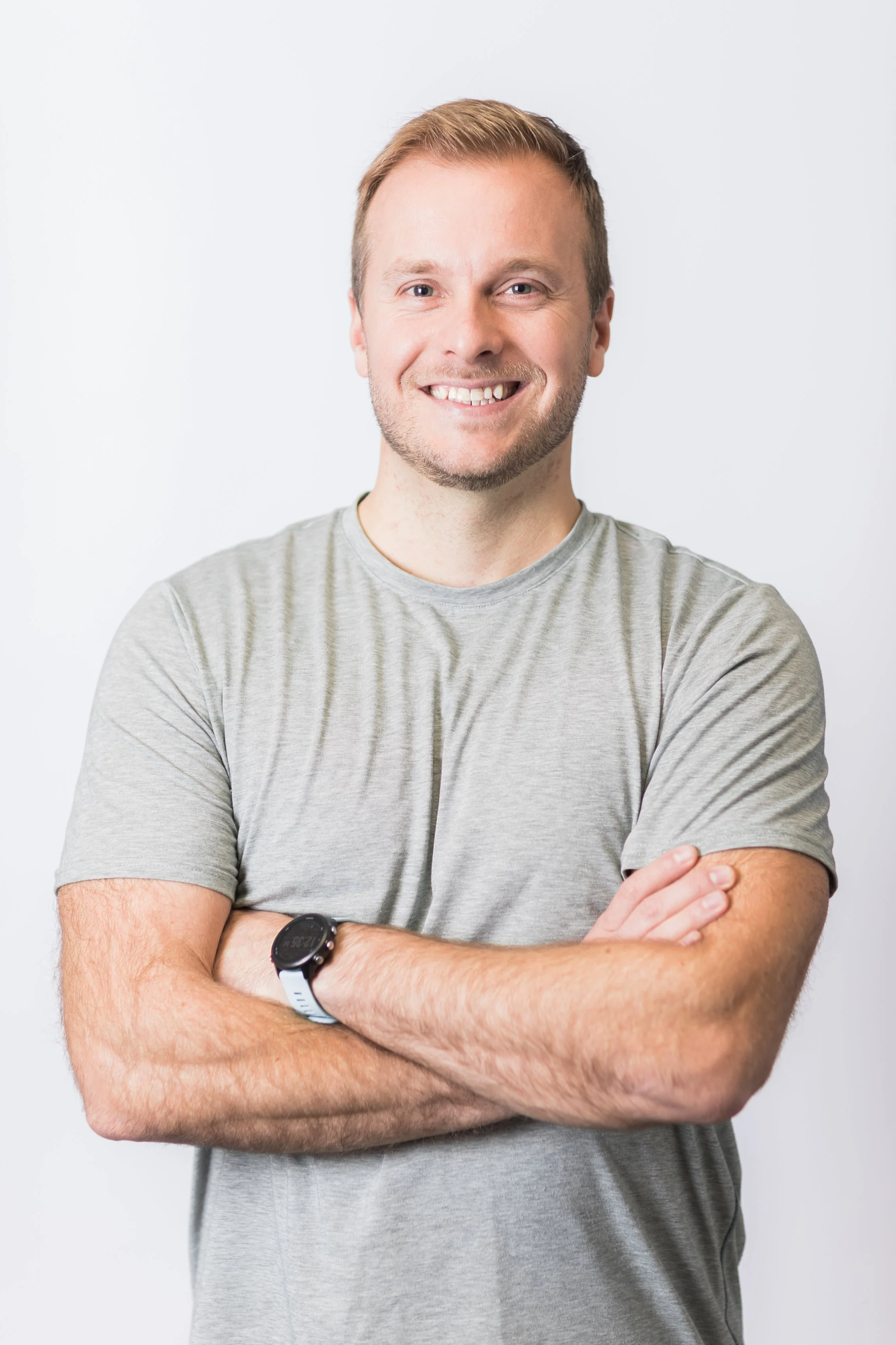 Kevin Berardinelli: A smiling man with short hair, wearing a light gray T-shirt and a smartwatch on his left wrist, crossing his arms against a plain white background.