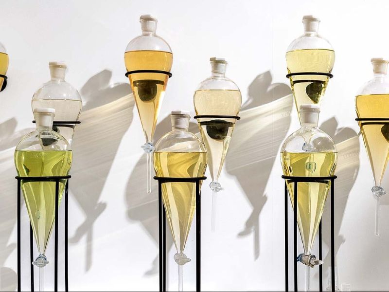 Multiple hanging glass vessels filled with different shades of liquids, supported by black metal stands, casting shadows on a white background.