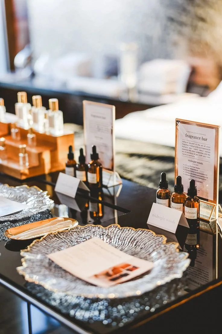 A display of amber glass bottles and fragrant oils at a fragrance bar, with informational signs and decorative trays.