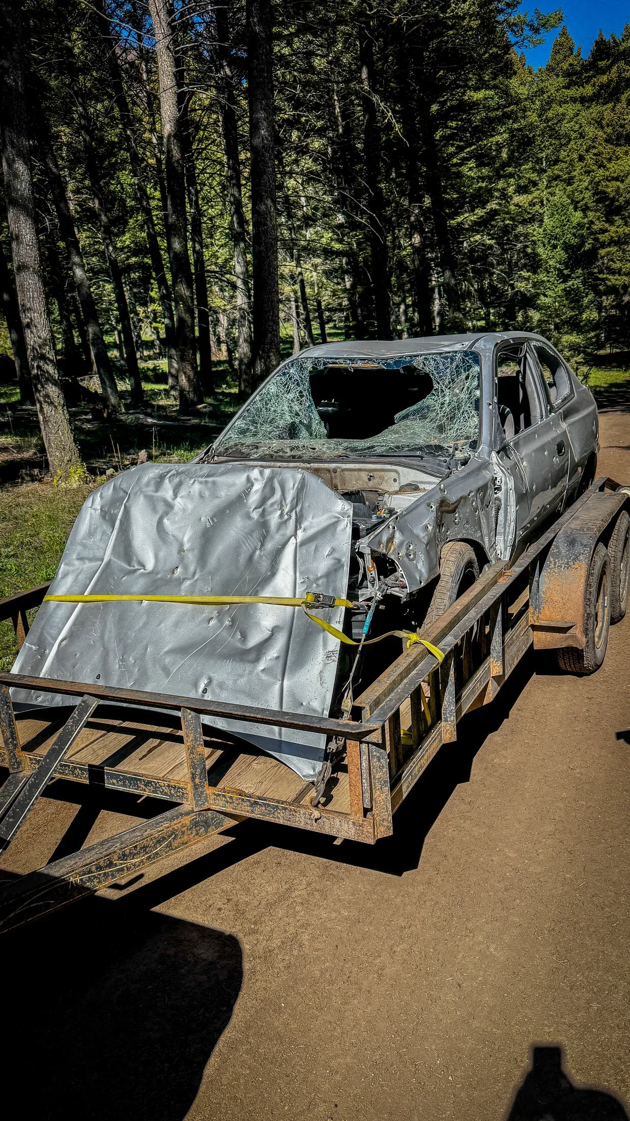 Shot-up dumped car strapped to a trailer during a 406 Cruisers public-land cleanup