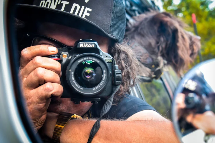 Aaron taking a photograph with a Nikon camera reflected in a vehicle mirror