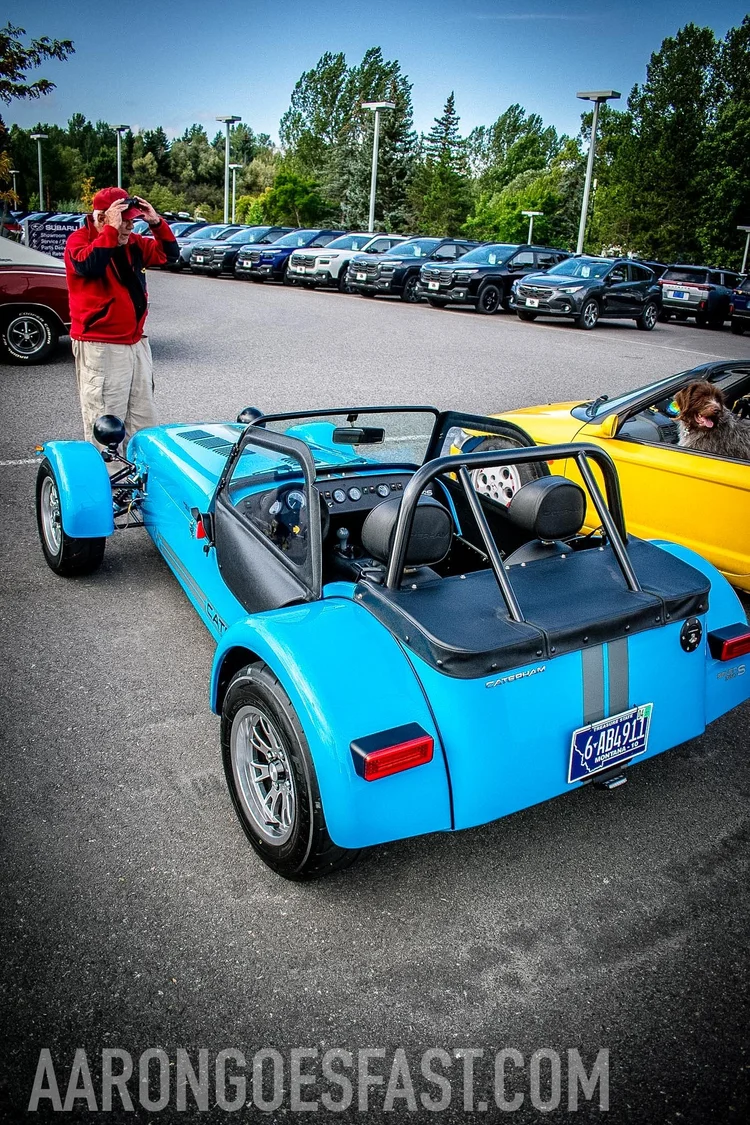 Rear three-quarter view of the blue Caterham Seven 360 with its owner and Aaron's dog Boone in the yellow Honda Beat nearby