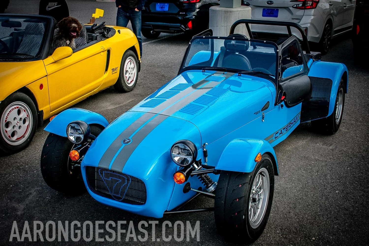 Blue Caterham Seven 360 parked next to Aaron's yellow Honda Beat and his dog Boone at a Bozeman car show